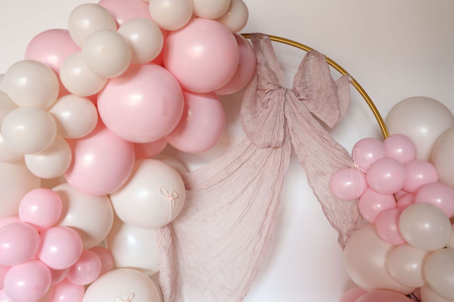 Pink and white balloon arch backdrop with delicate tulle draping and gold circular frame.