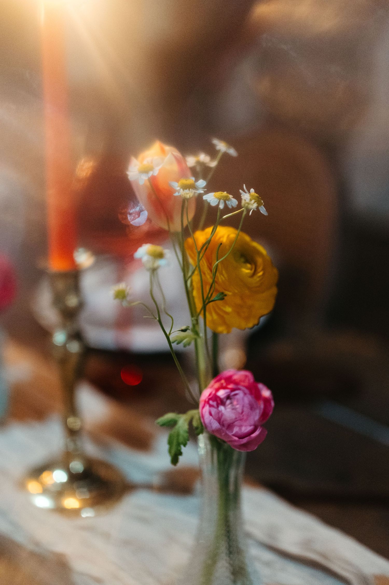 Delicate floral arrangement with yellow ranunculus and pink roses in a vase with soft candlelight atmosphere.
