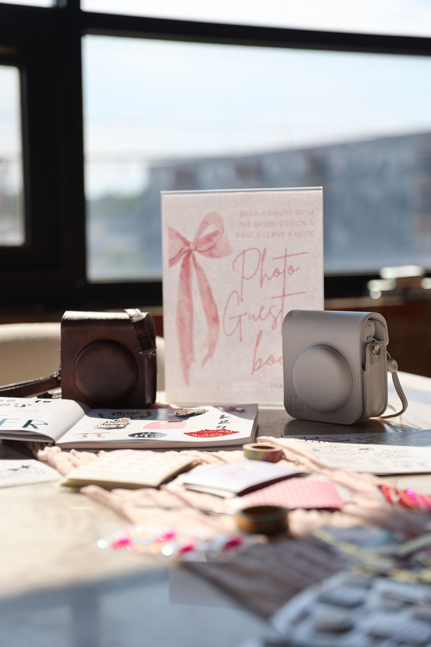 Wedding photo station setup with instant cameras and a pink bow decorated card on a sunny table.