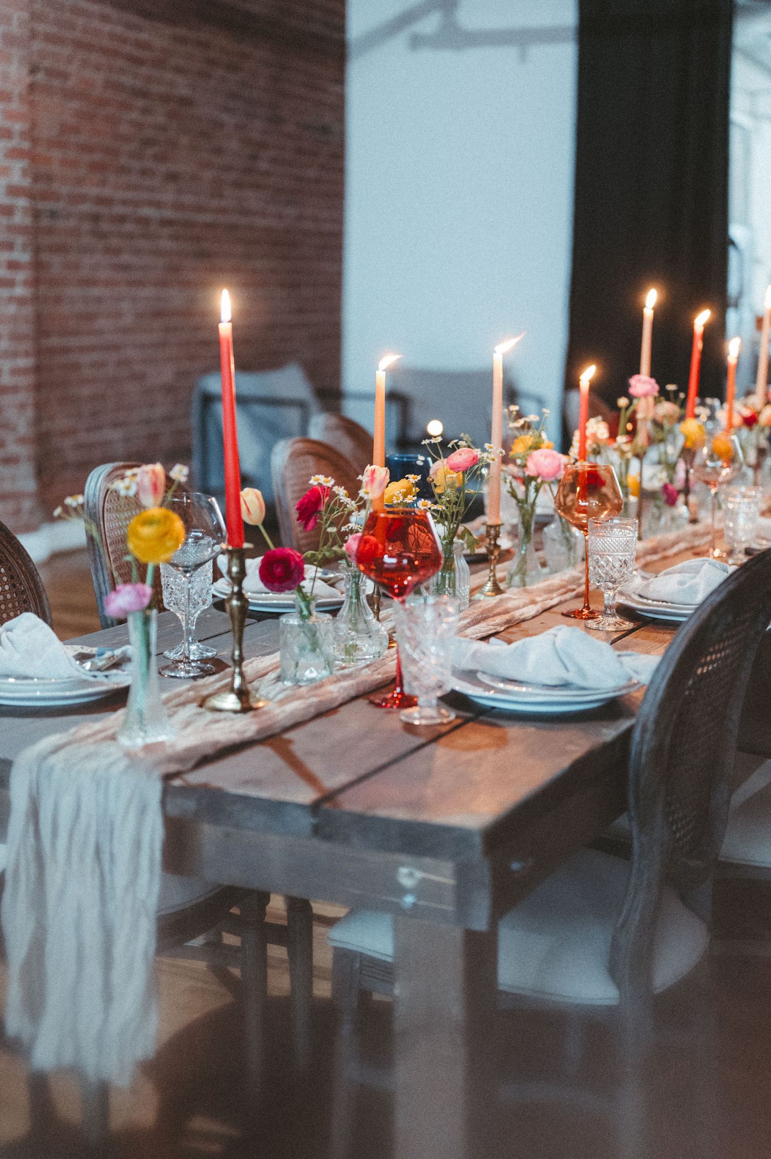 Romantic table setting with red taper candles and colorful floral centerpieces in mason jars.