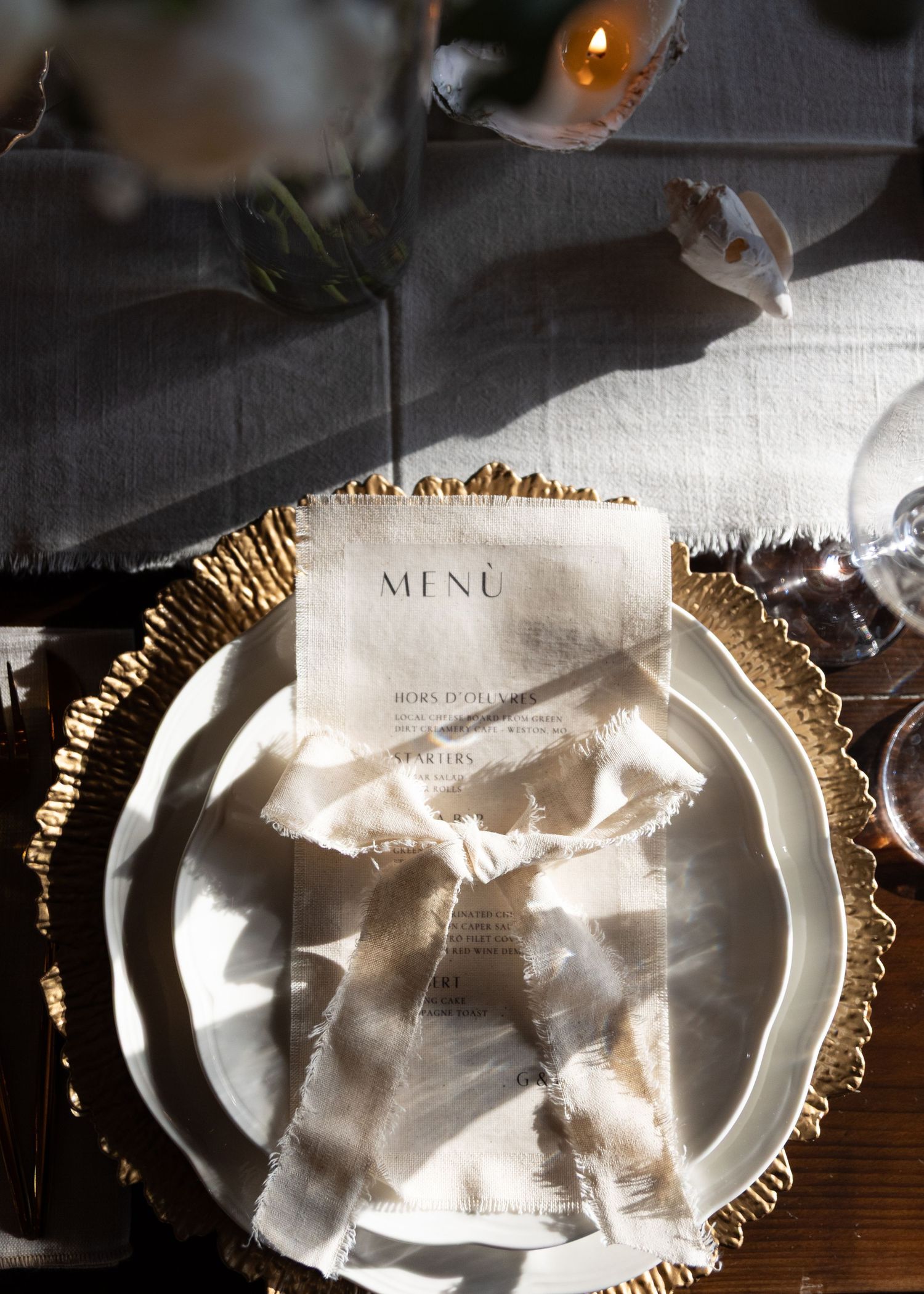 Elegant place setting with gold charger plate and menu card on white tablecloth.