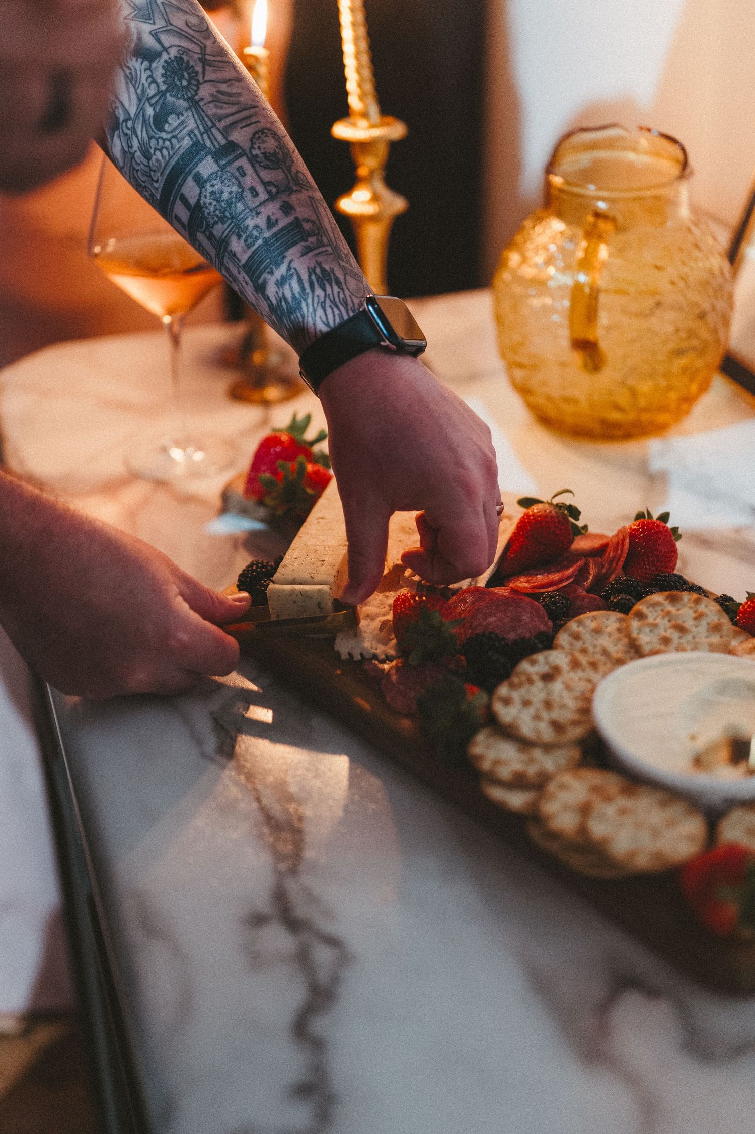 Tattooed hand arranging food on a serving platter next to an amber glass container.