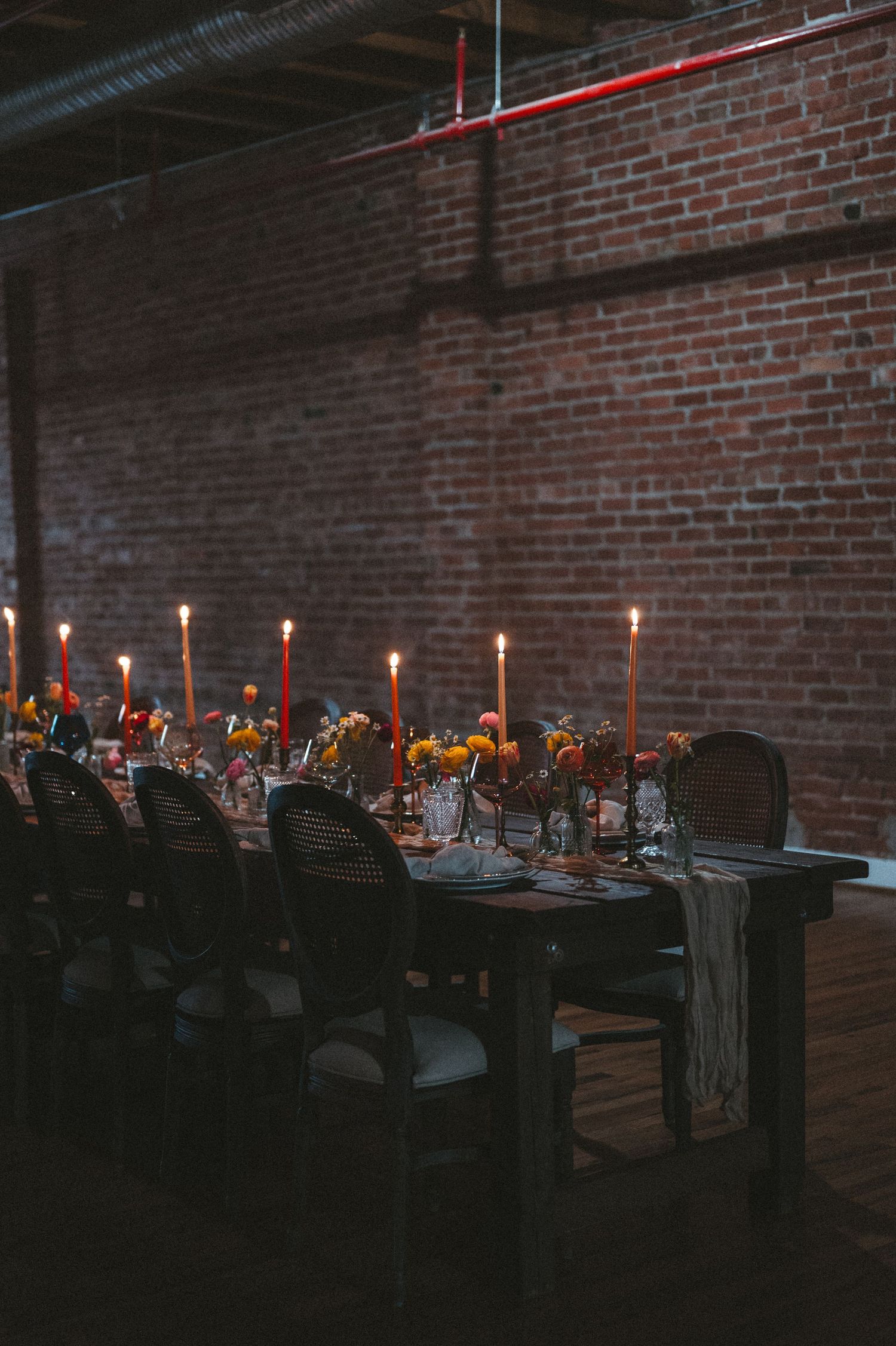 Moody candlelit dining table setup in brick-walled industrial space.