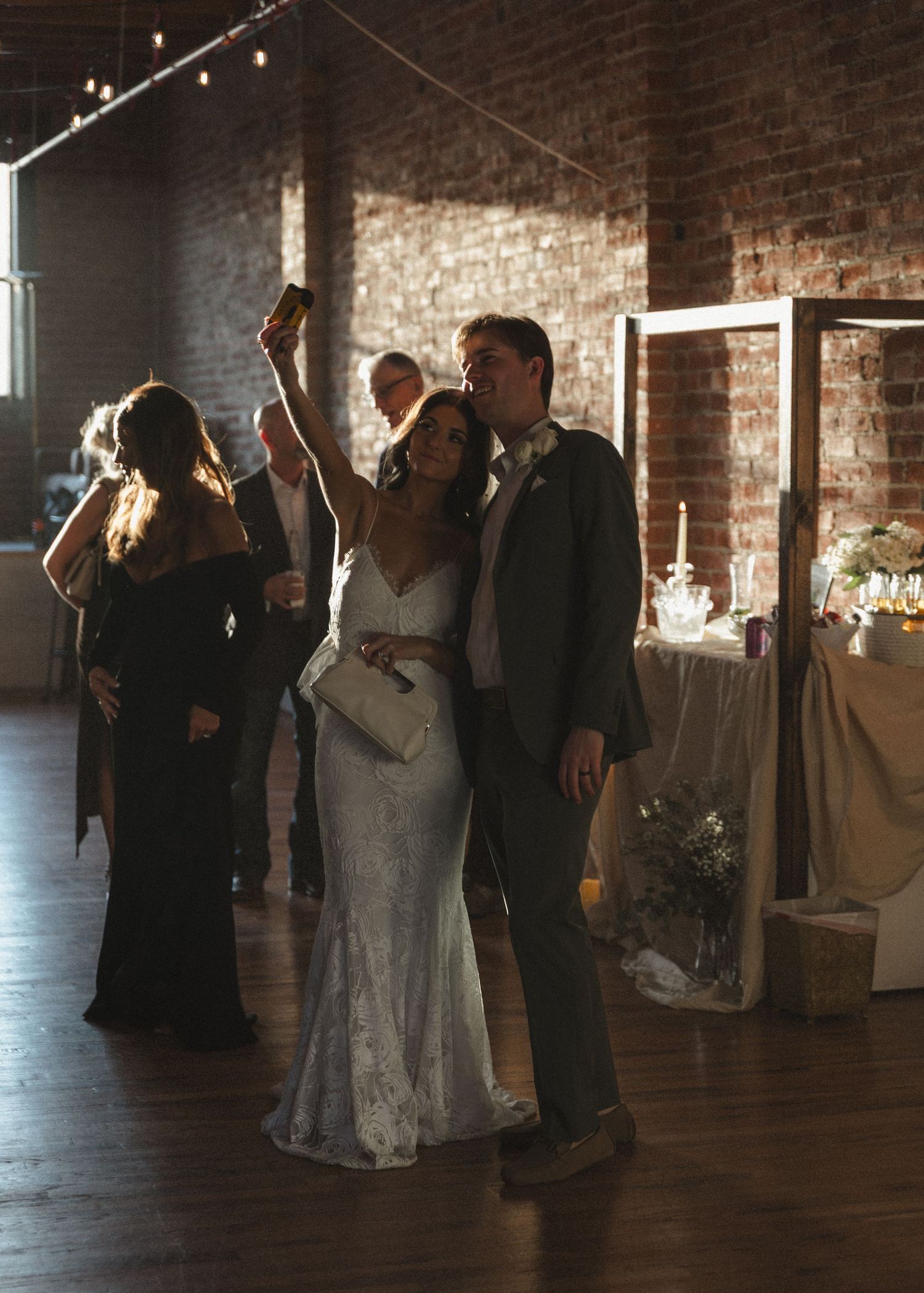 Wedding celebration in industrial venue with exposed brick walls and string lights overhead.