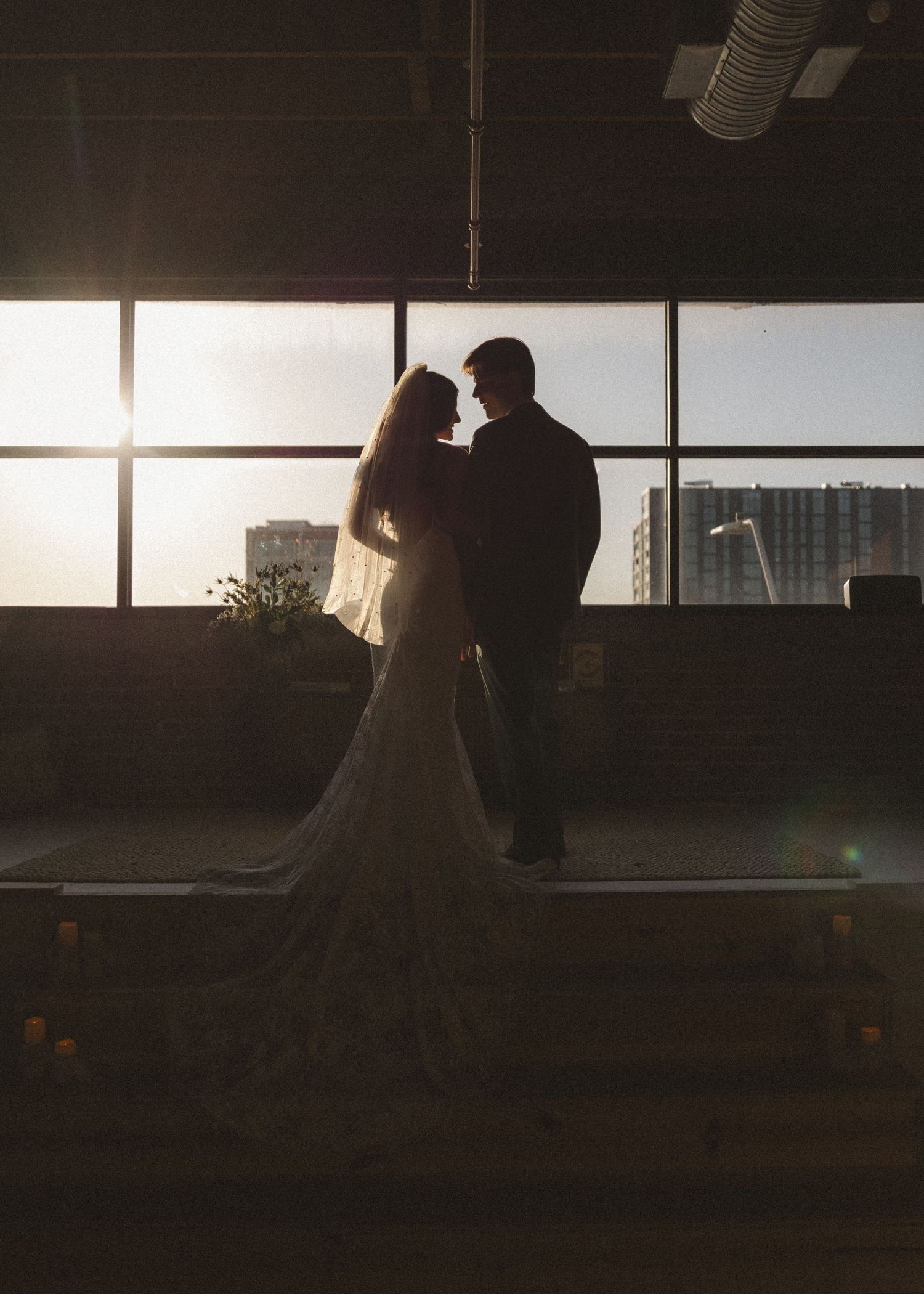Backlit wedding couple in an intimate moment against bright windows in an industrial space.