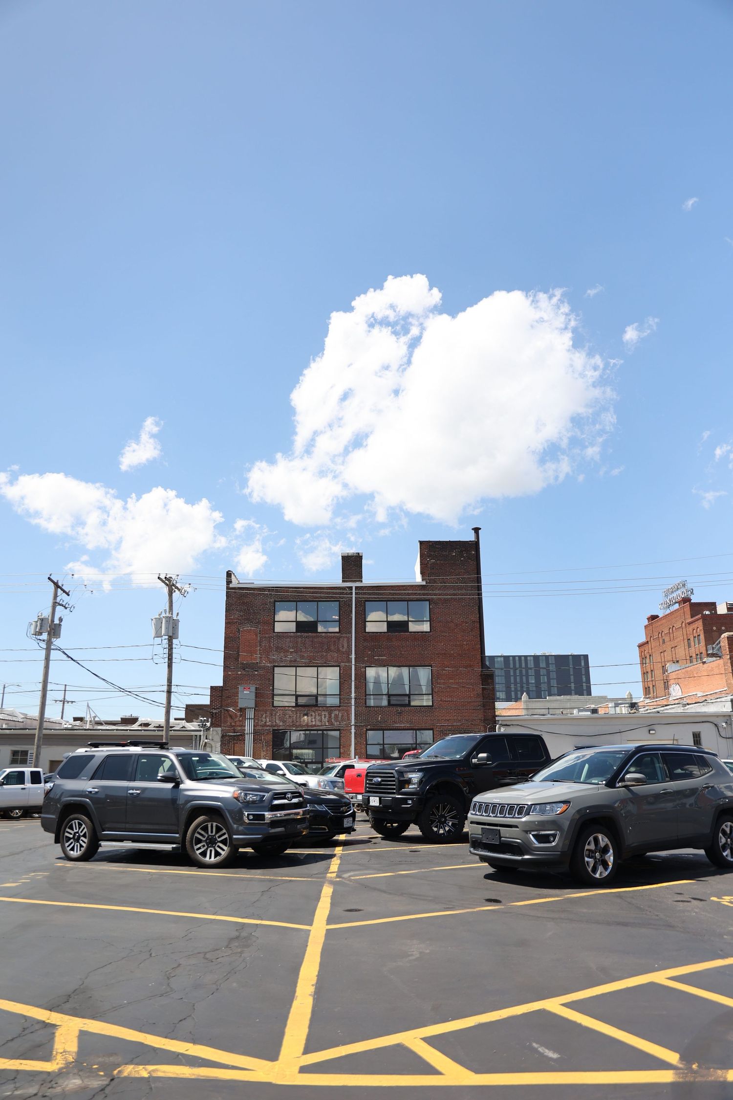 Parking lot with SUVs and brick building under blue sky with white clouds.
