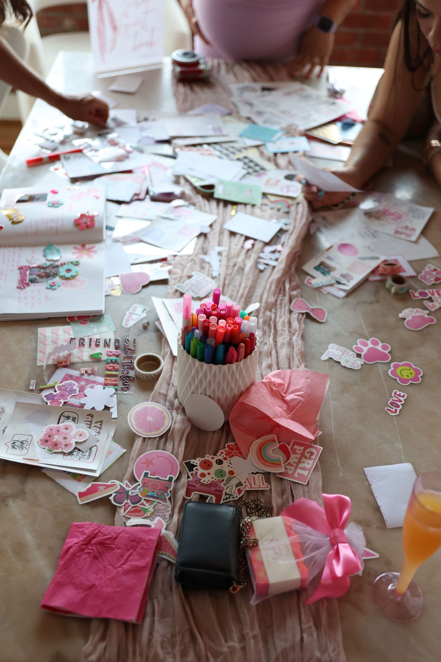 Party supplies and decorations scattered on table with pink gift bags and markers.