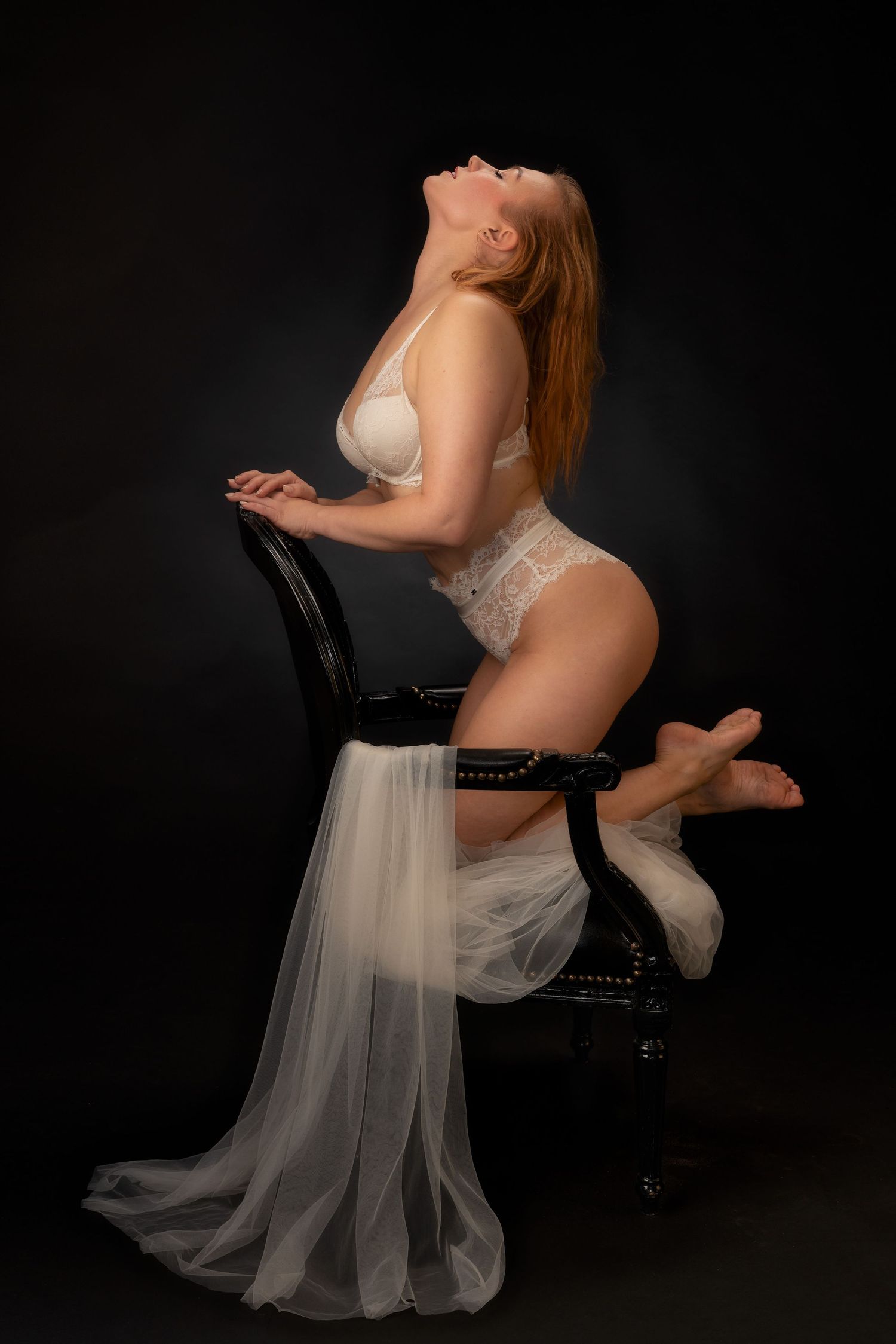 Boudoirkuva studiolla mustaa taustaa vasten. Nainen valkoisissa pitsialusvaatteissa.