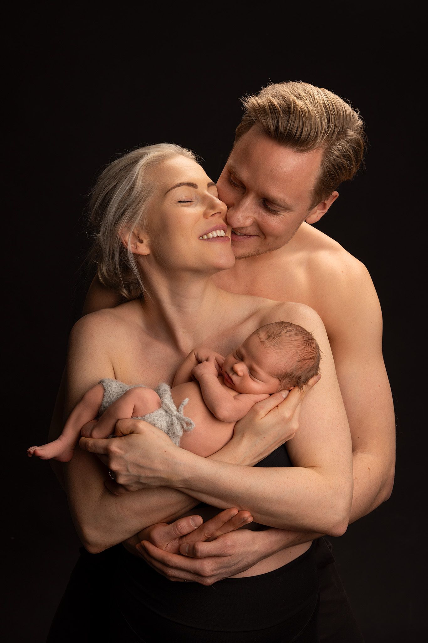 Vastasyntynyt vauva äidin sylissä. Äiti ja isä hymyilevät onnellisina toisilleen.