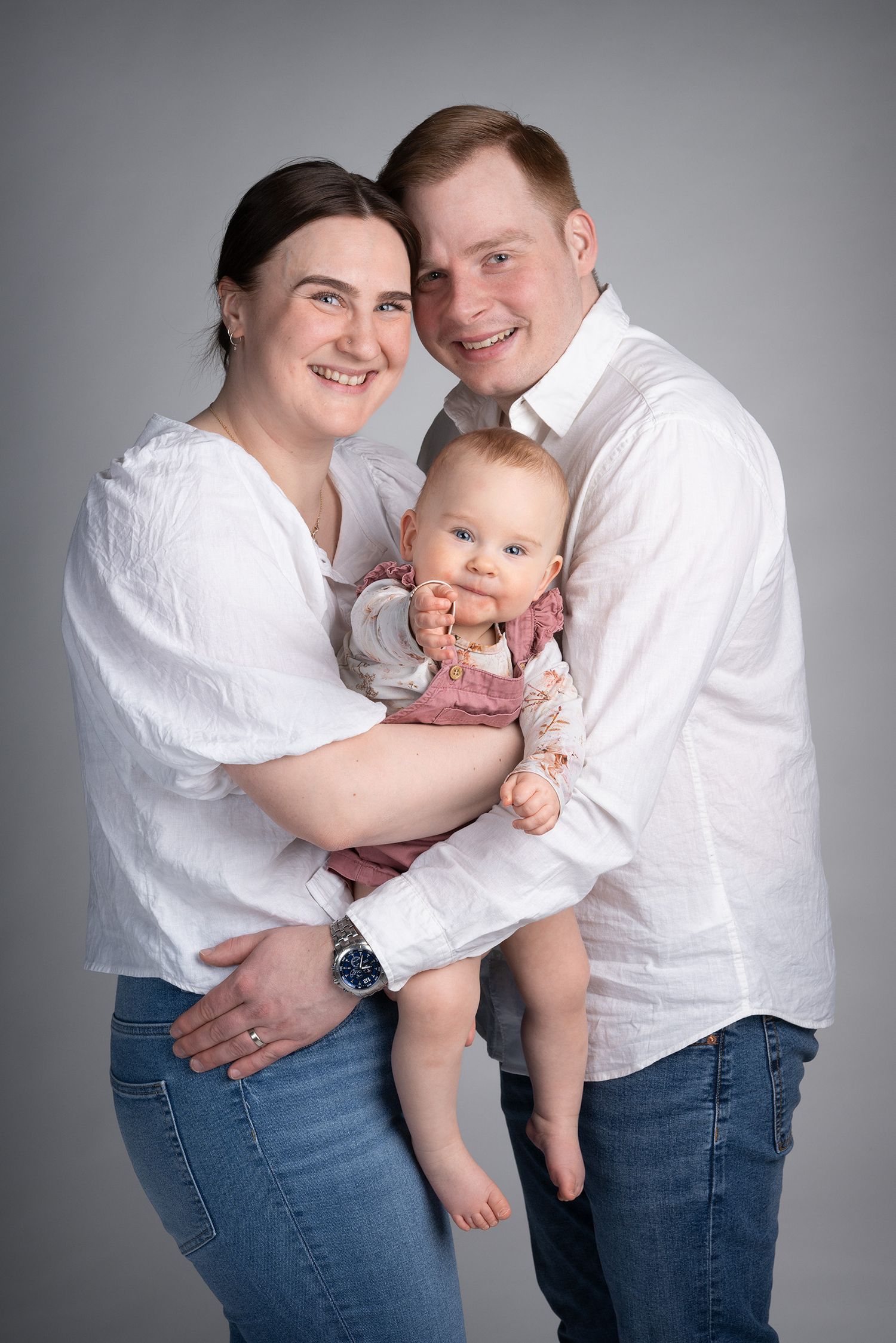 Iloinen ja naurava perhe joilla on yhteensopiva vaatetus farkuista ja vaaleista paidoista.
