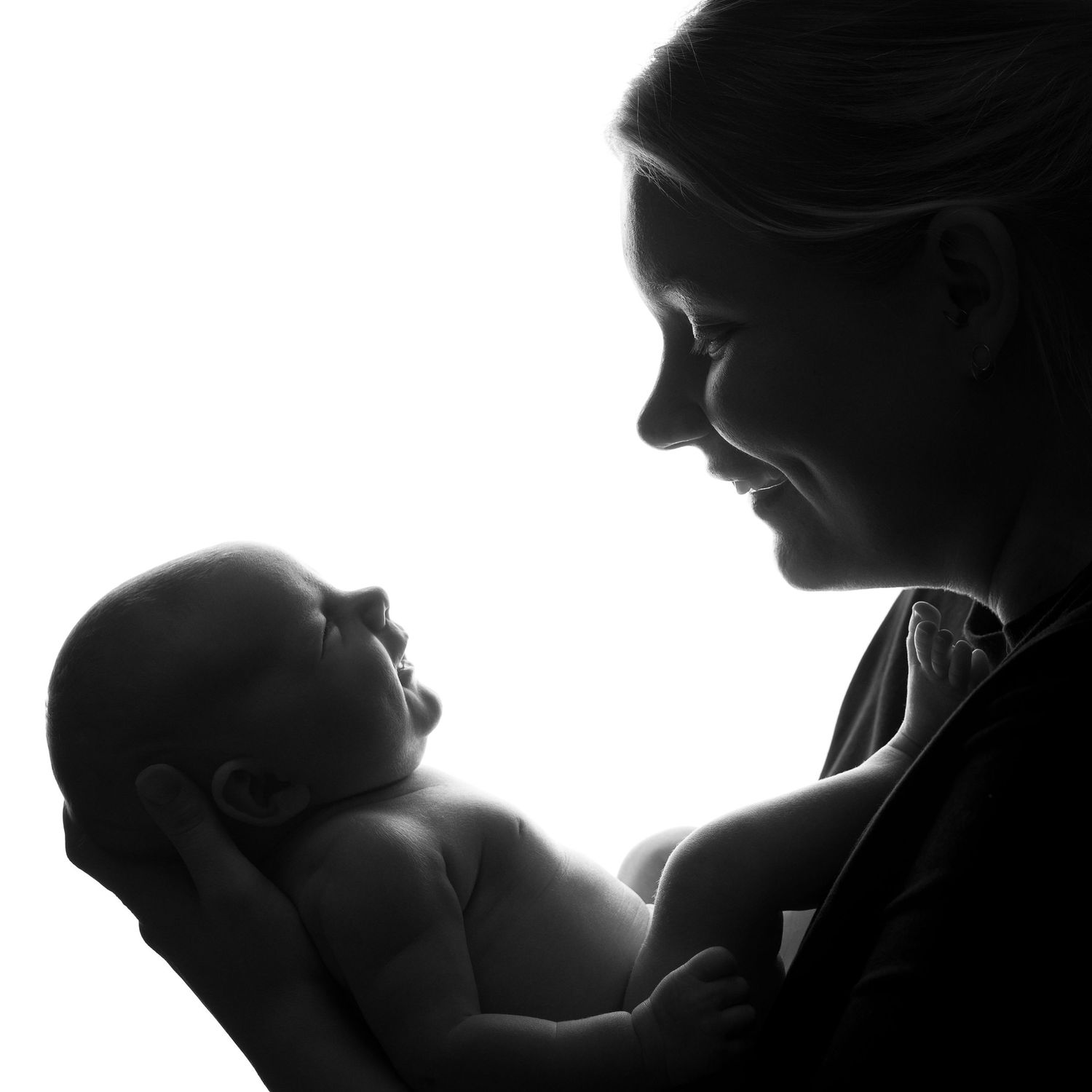 Mustavalkoinen siluettikuva äidistä ja vastasyntyneestä vauvasta jossa molemmat hymyilevät toisilleen.