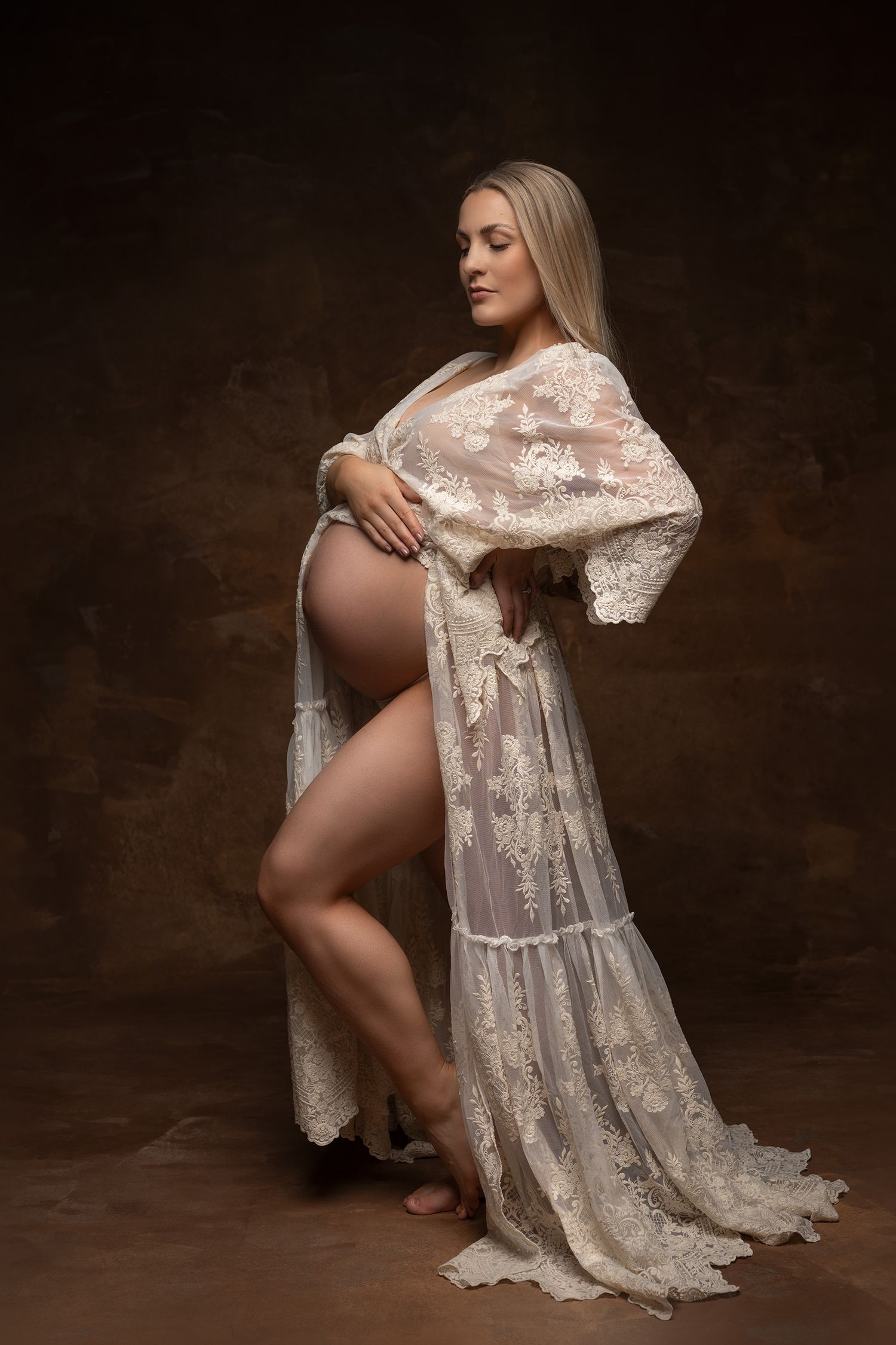 Elegantti raskausajan kuva jossa tumma tausta ja naisella vaalea boho-henkinen pitsimekko joka paljastaa vatsan.