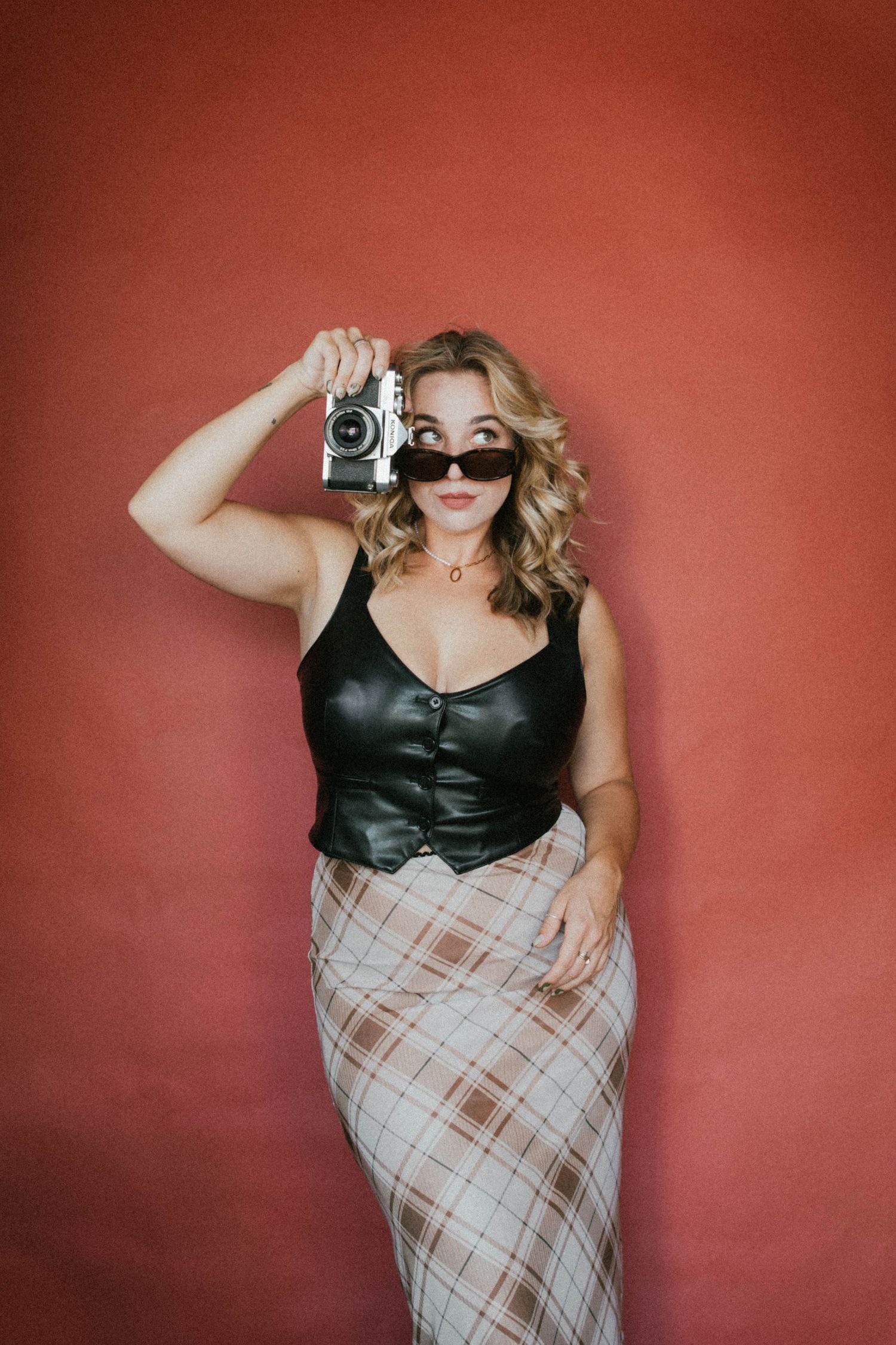 Blonde woman in black leather top and plaid skirt holding vintage camera. Photos by Beck based in SLO, CA. Rebecca Sligh