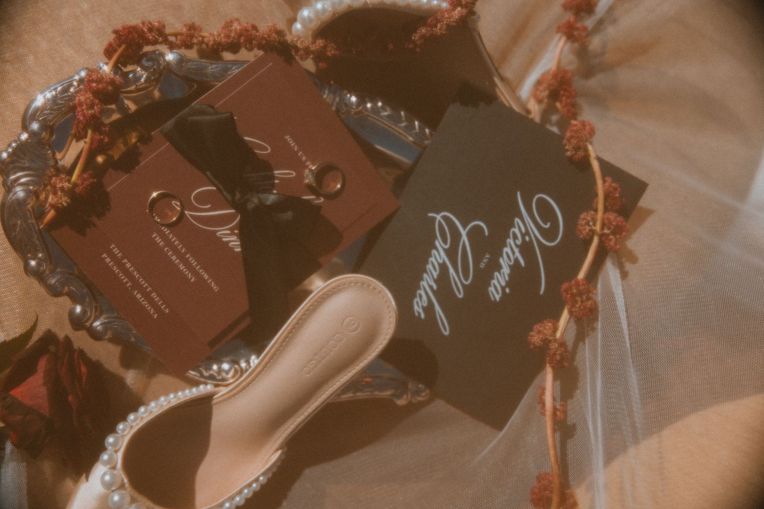 Elegant dark wedding stationery, rings, bridal heels, and floral details styled in a flat lay.