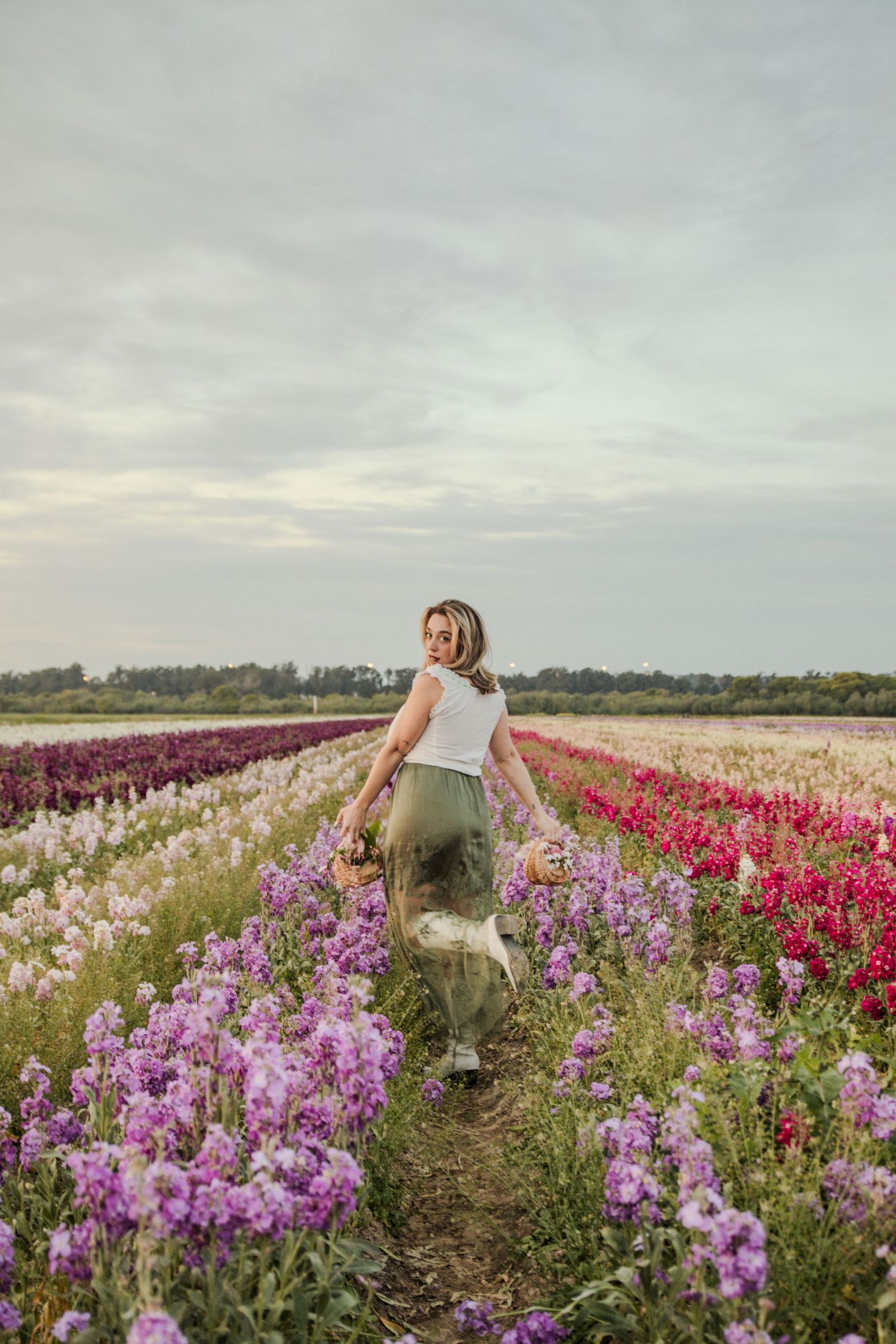 Rebecca walking through colorful flower fields with pink and purple blooms under cloudy sky. Photos by Beck based in SLO, CA.