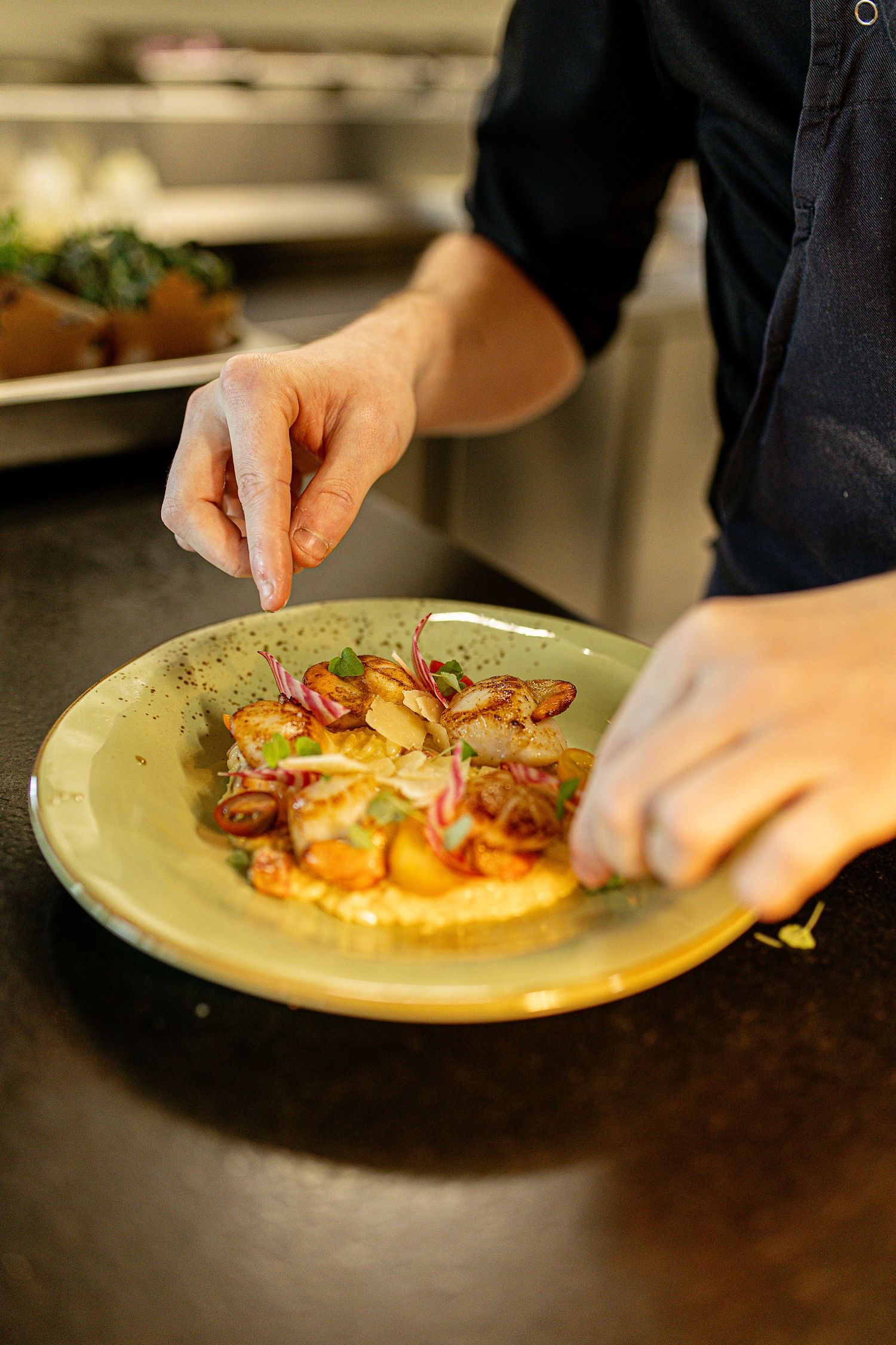 Photo d’un cuisinier en action, dressant un plat avec précision et soin, ambiance de cuisine professionnelle et créative.