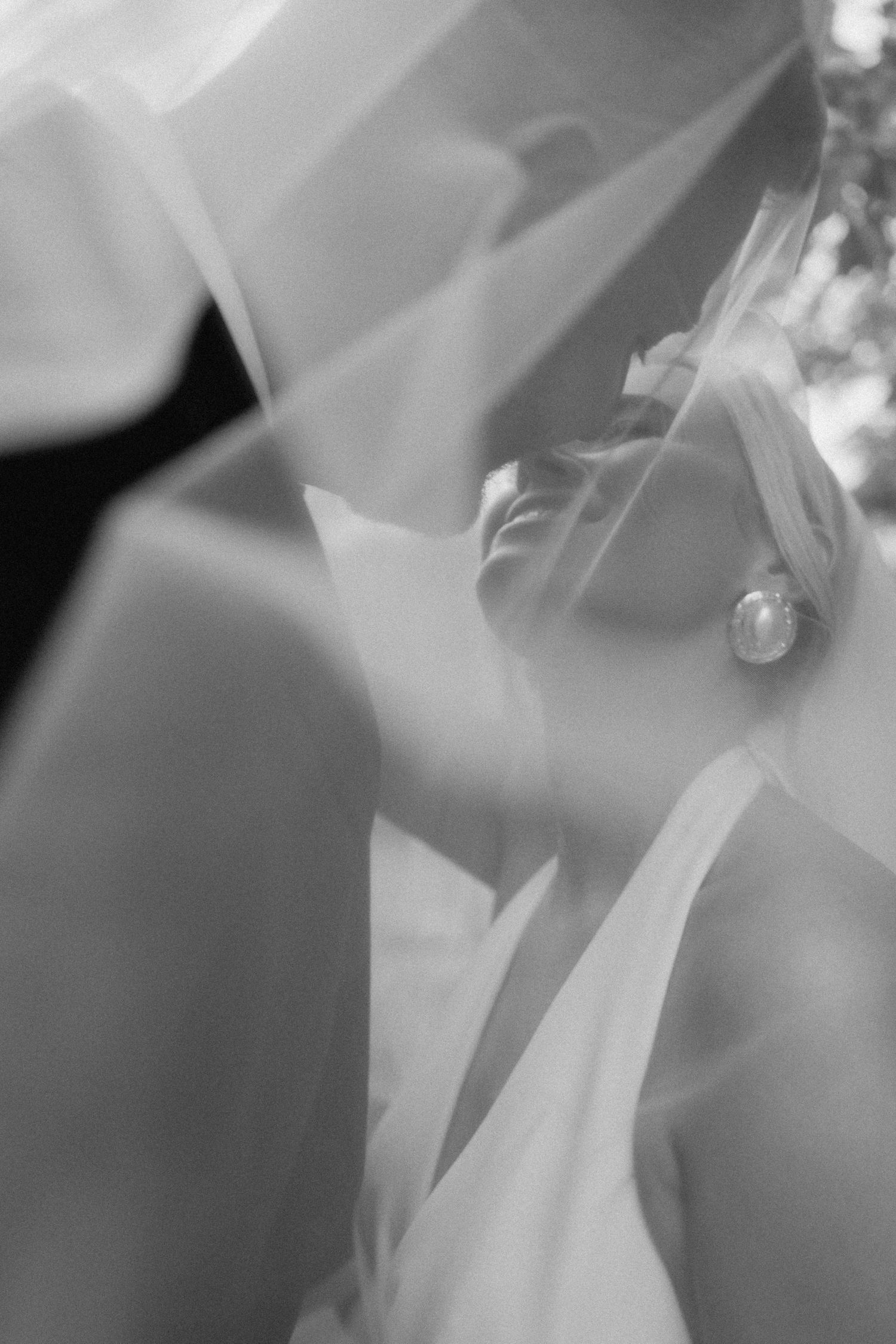 Black and white photo of a bride under her veil, showcasing elegant earring and wedding dress details.