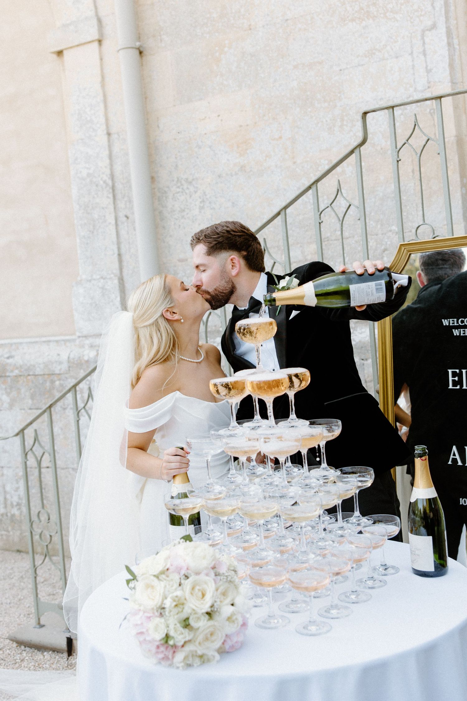 Bride and groom kissing beside a champagne tower at their elegant outdoor wedding reception.