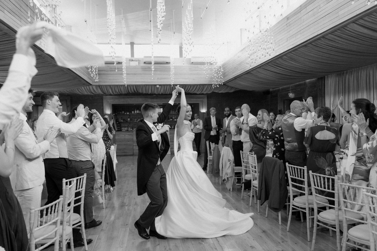Bride and groom share first dance surrounded by cheering guests at elegant wedding reception.