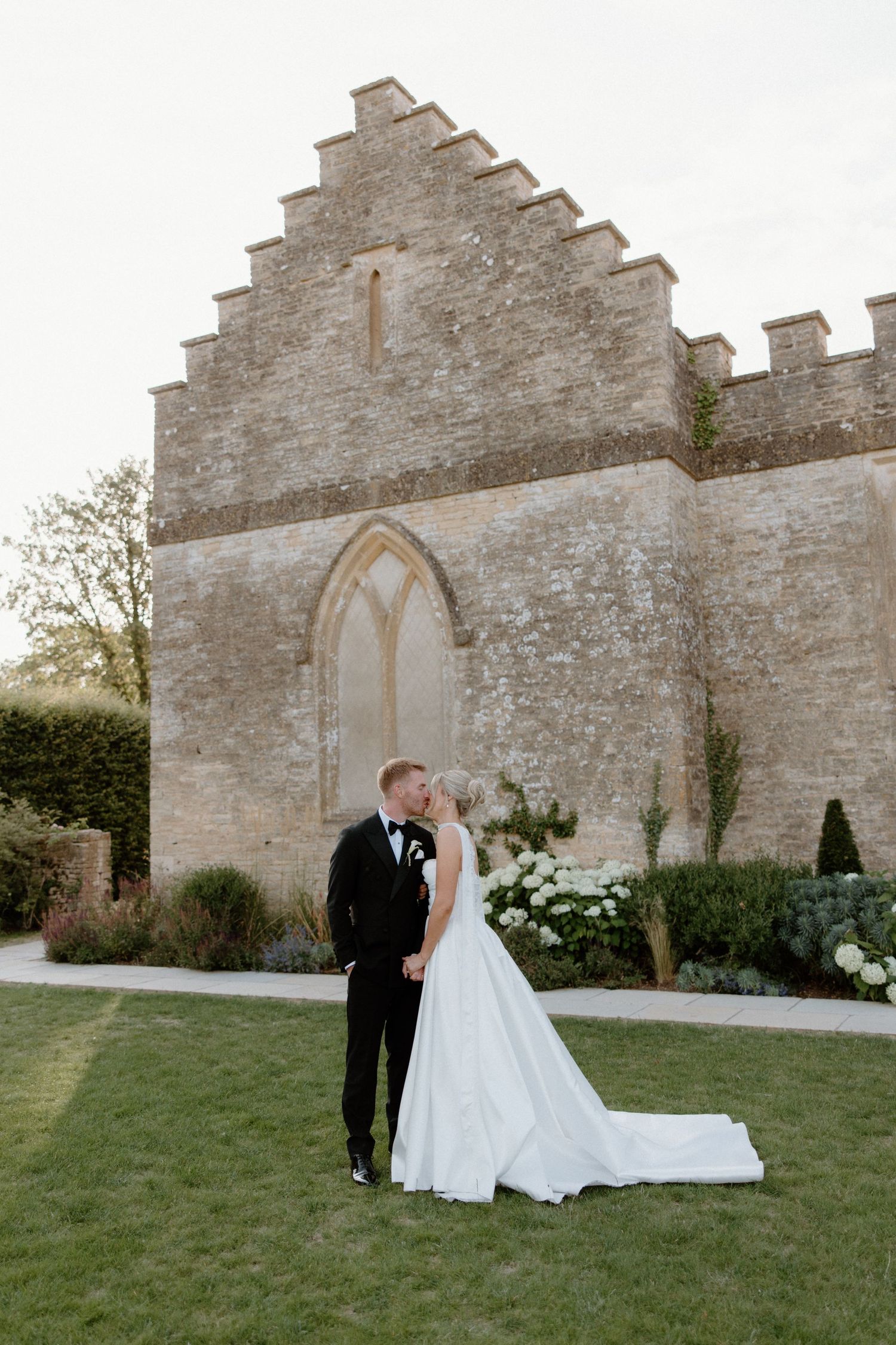 Bride and groom kissing in front of a historic stone chapel at a elegant outdoor wedding venue.