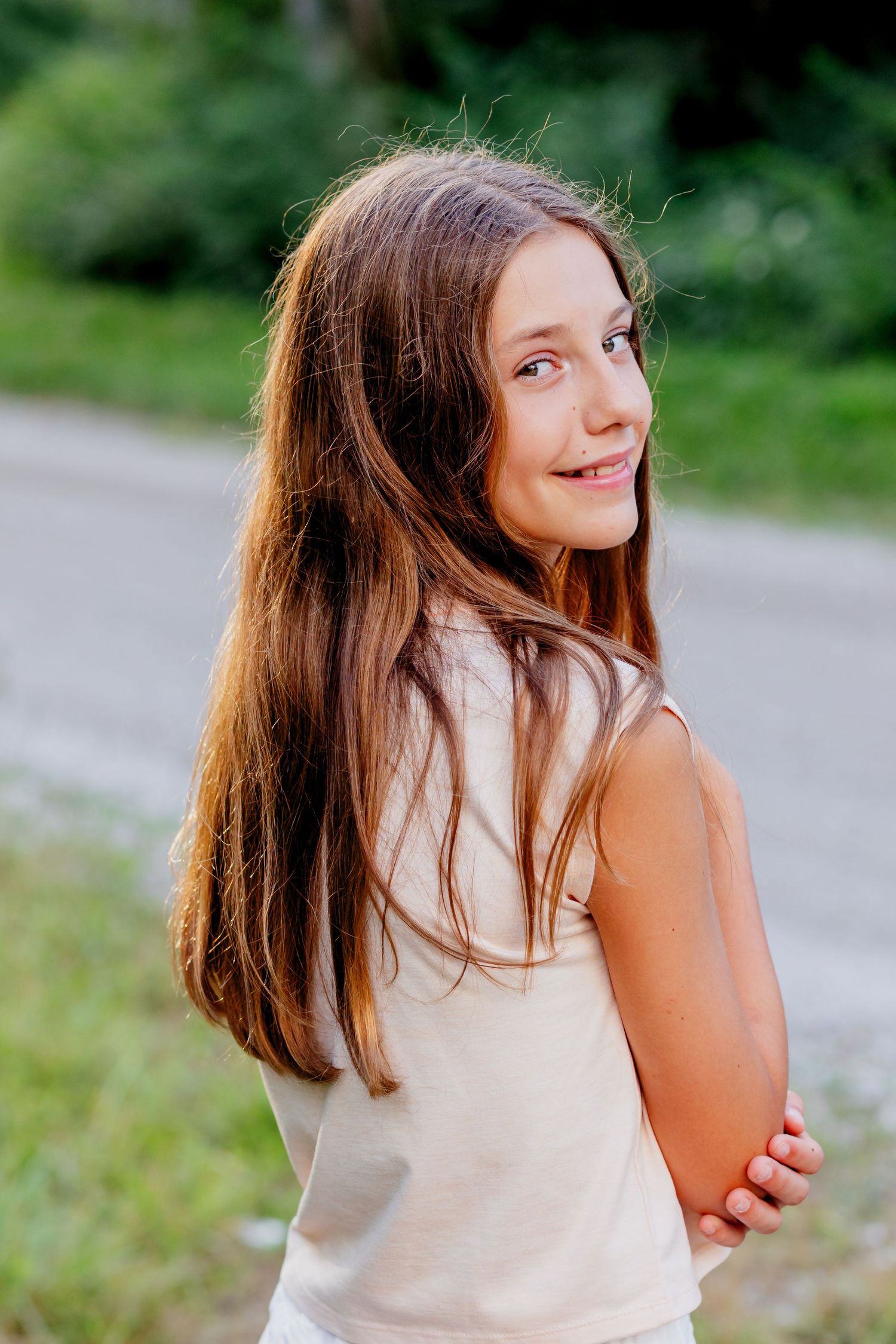 Natural portrait of someone with long brown hair glancing over their shoulder on a path.