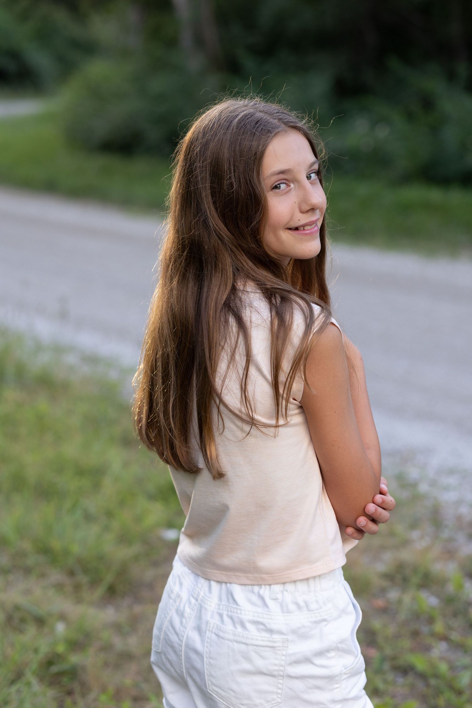 Portrait of a long-haired person in cream top posing outdoors on a path.