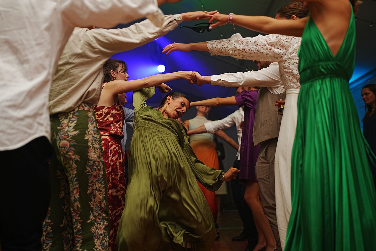 Colorful dresses create a vibrant pattern as wedding guests dance in a line.