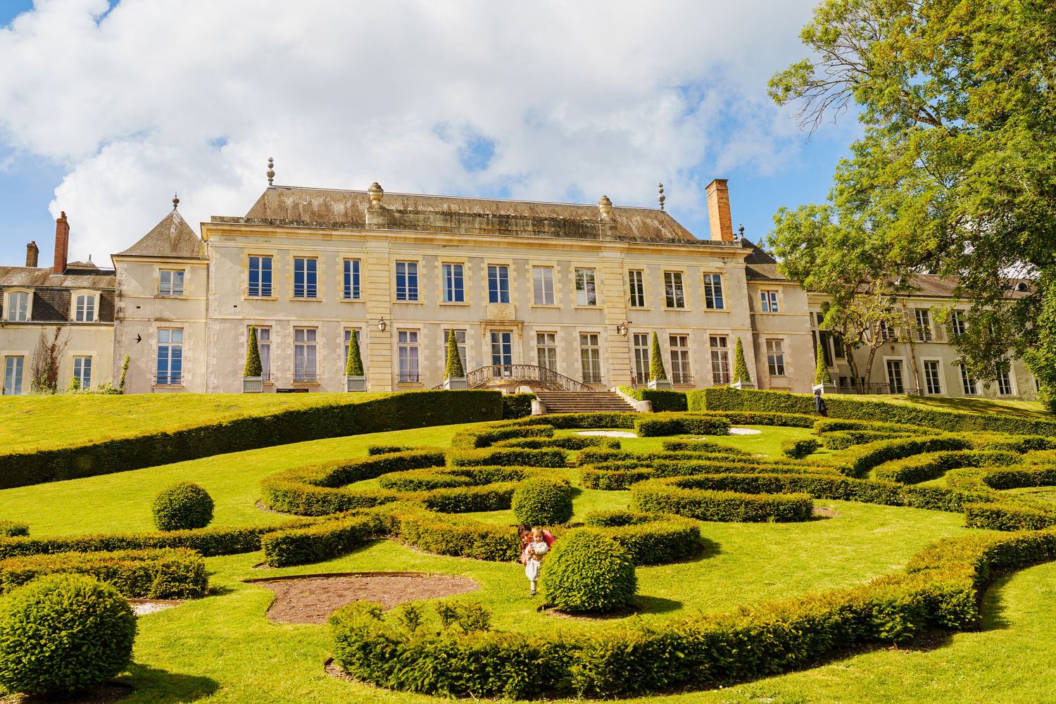 Elegant French chateau with manicured topiary garden featuring geometric boxwood hedges on a sunny day.