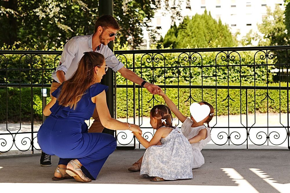 Family in coordinated outfits kneeling together on a patio with decorative iron railings in the background.
