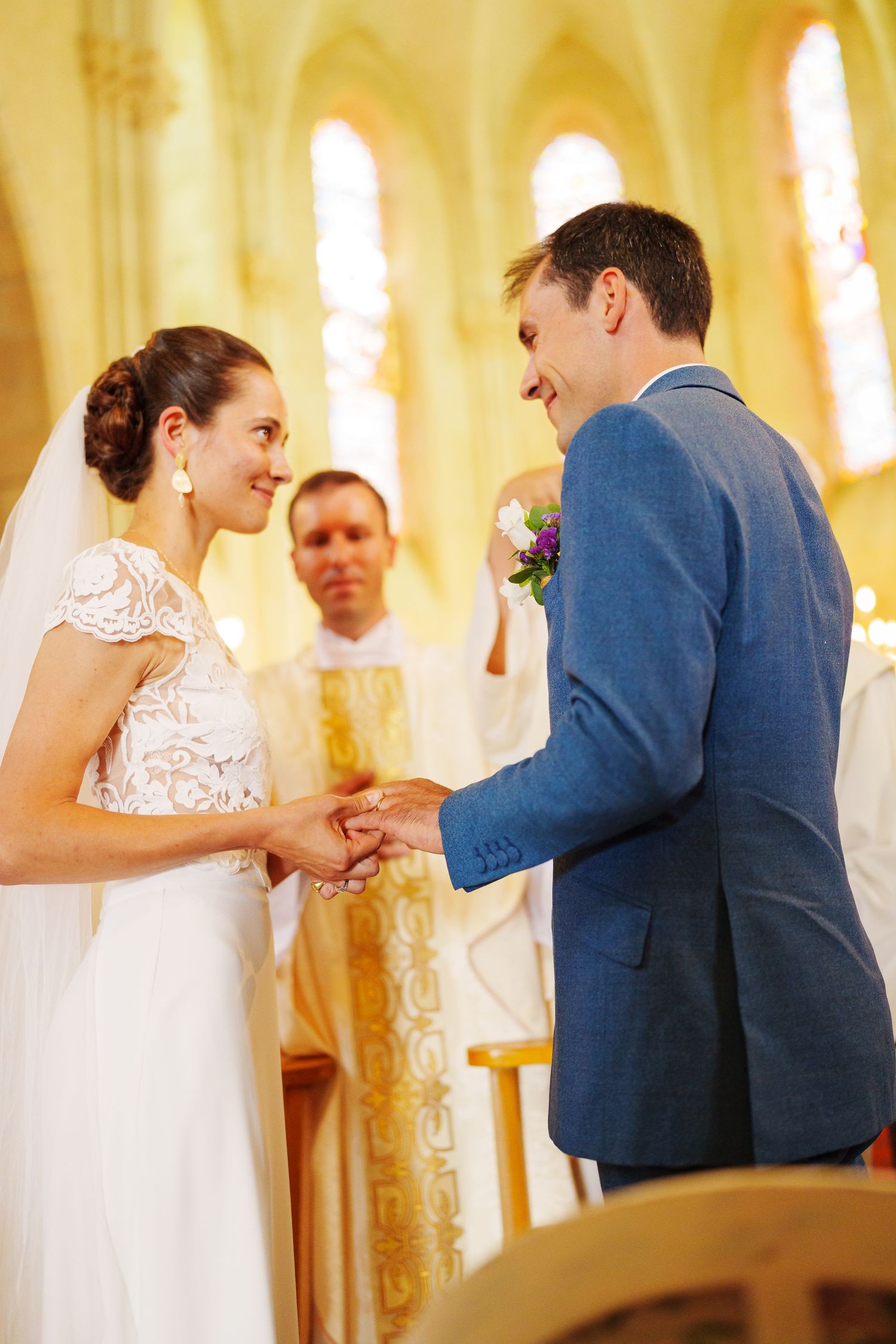 Exchange of rings during wedding ceremony in church with golden lighting.