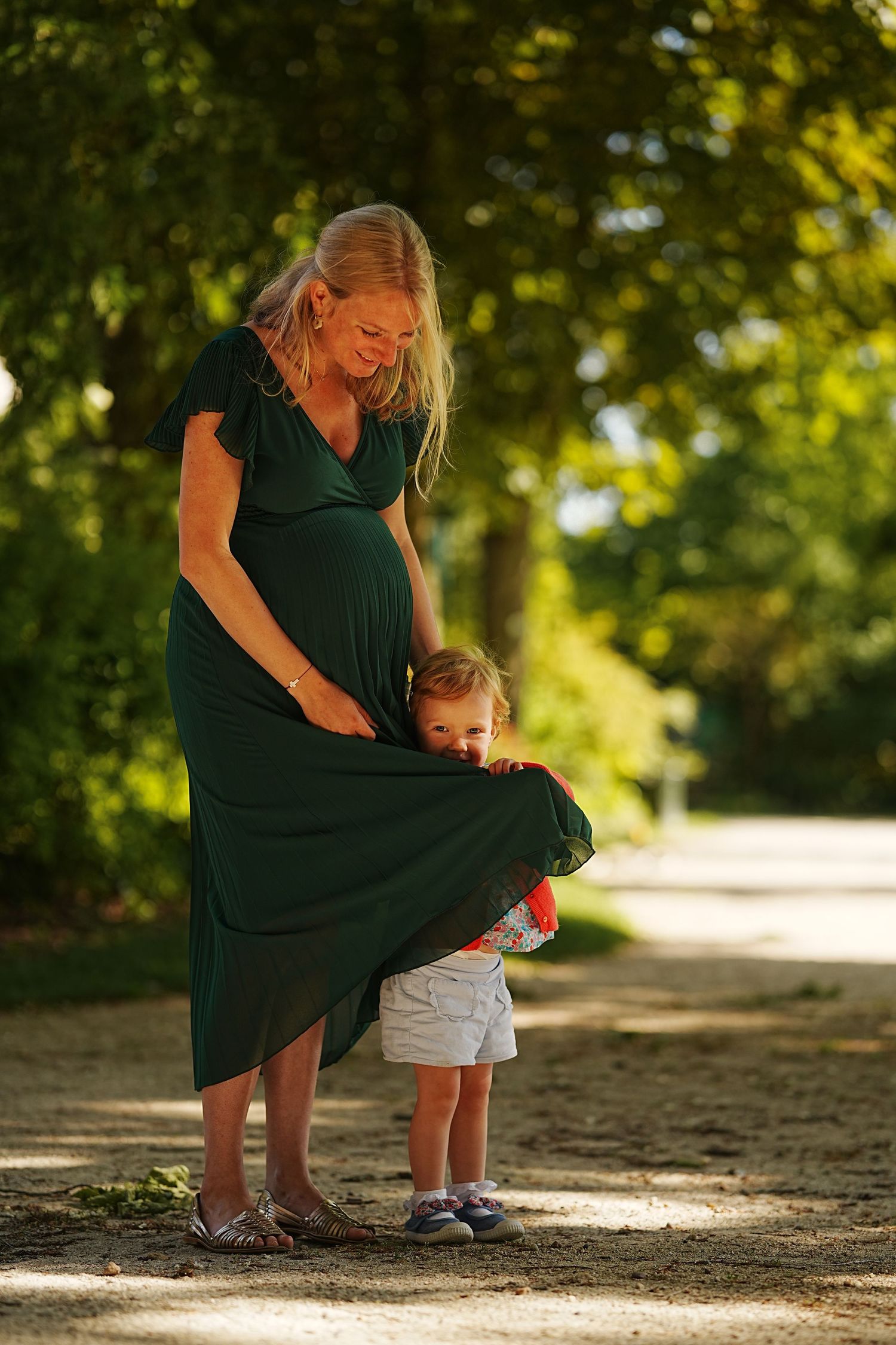 A tender outdoor moment between parent and child on a sunlit path.