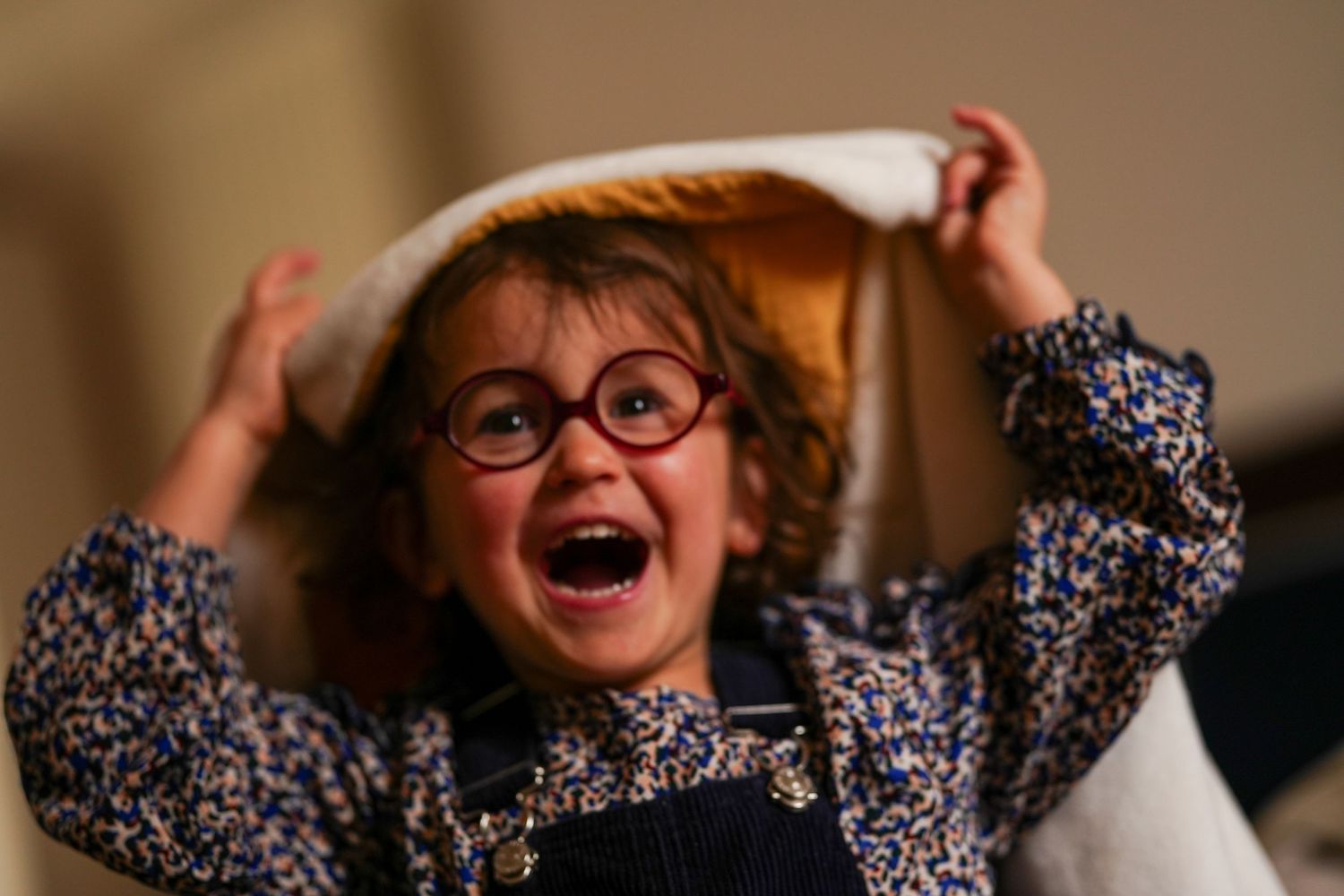 Excited child in glasses and floral shirt holding up hat.