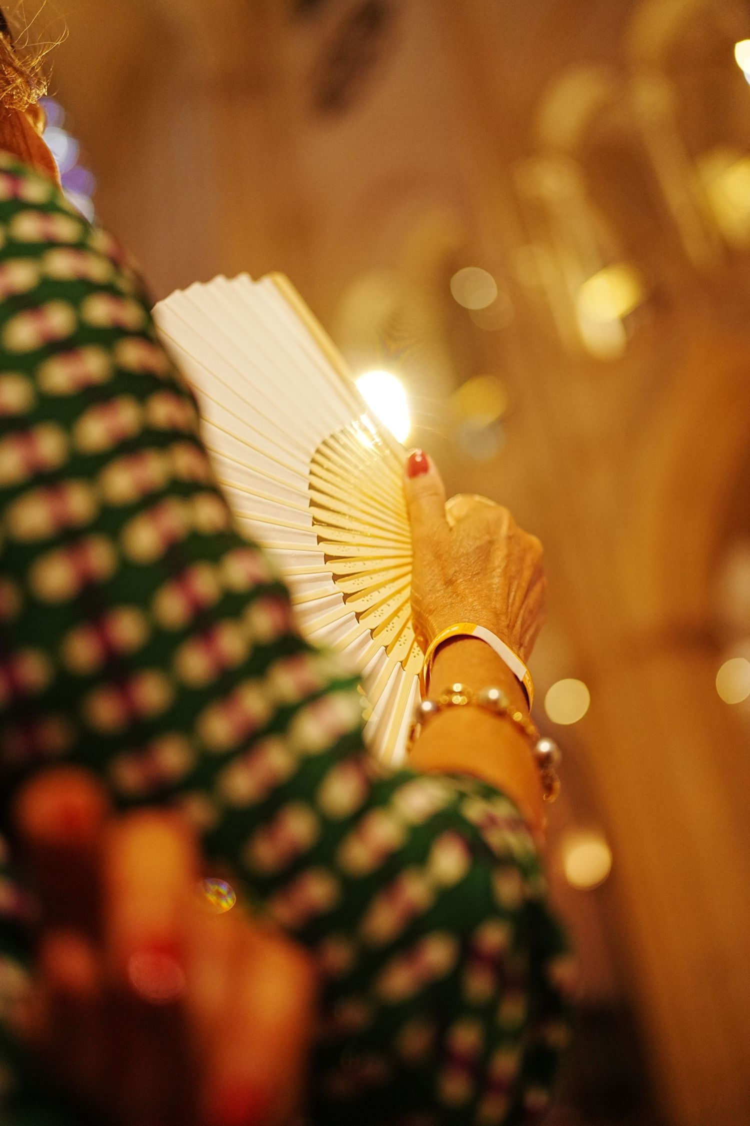 Decorative golden paper fan ornament with bokeh lights and Christmas tree in background.