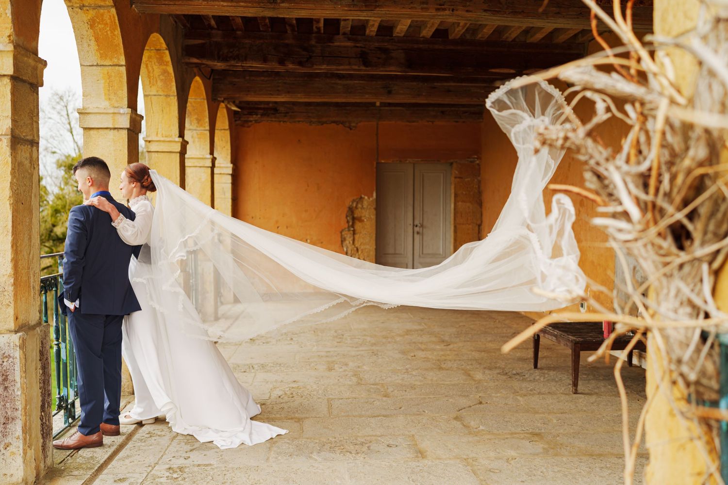 A white flowing veil creates a dramatic effect as it billows in the wind along a rustic wooden porch.