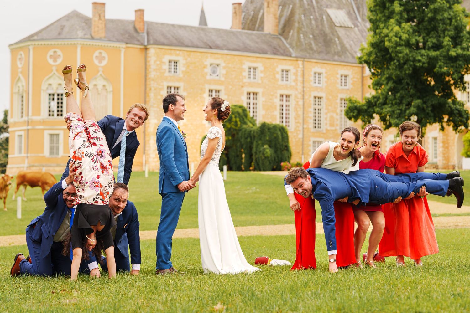 Wedding party in red attire poses playfully on the lawn of an elegant yellow mansion.
