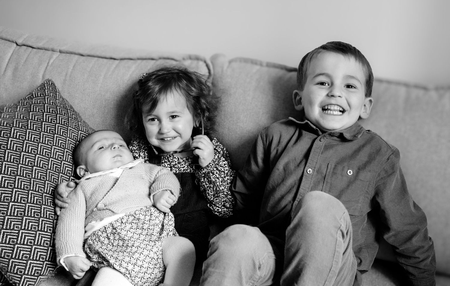 Black and white portrait of siblings sitting together on couch.