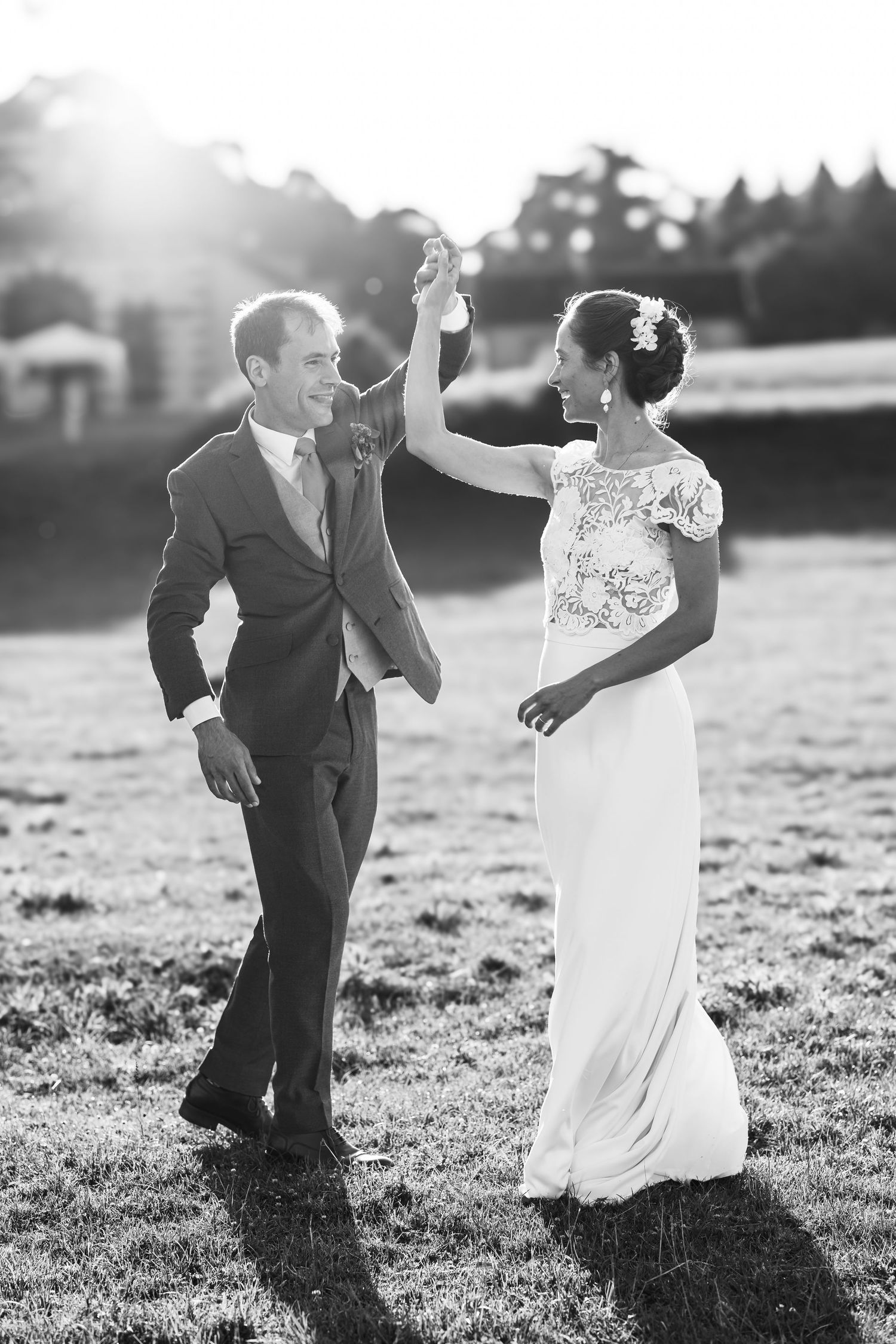Black and white photo of couple dancing playfully in a sunlit field.