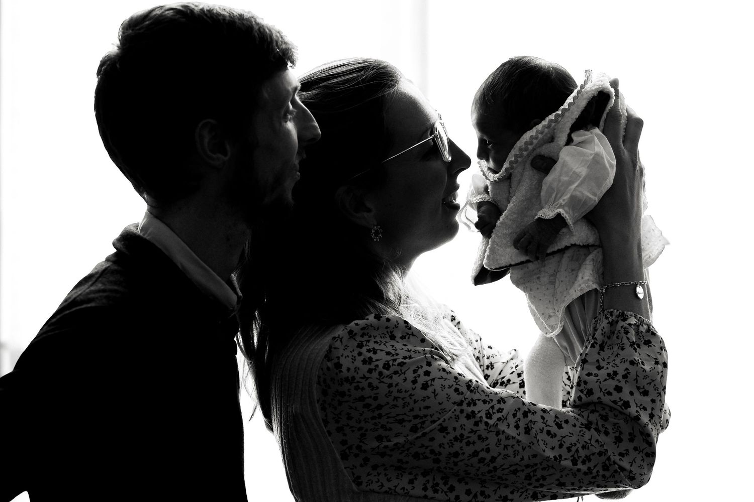Black and white silhouette of couple kissing while holding newborn baby in tender family portrait.