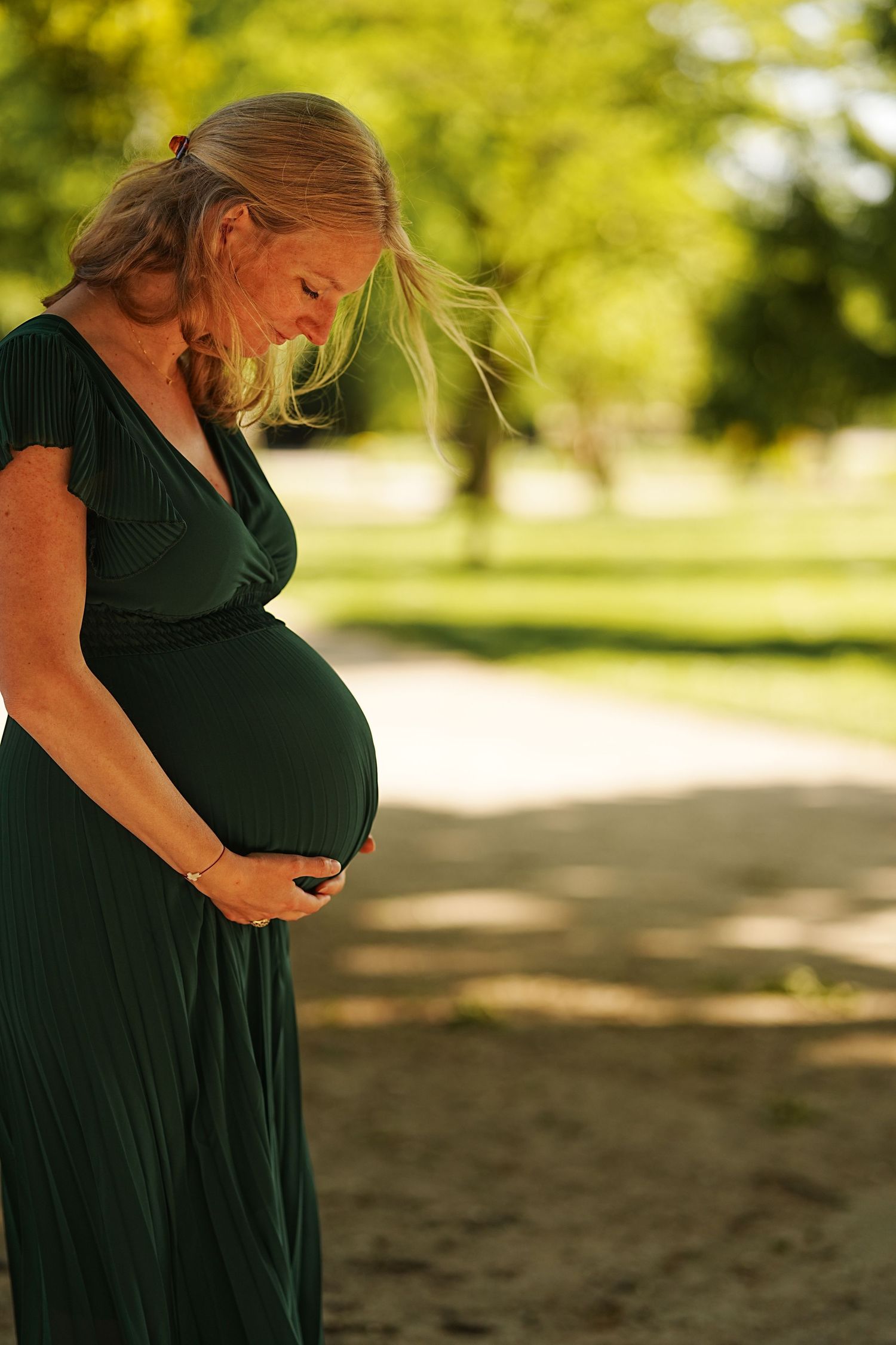 Outdoor maternity portraits of an expectant mother in a dark green dress at golden hour.