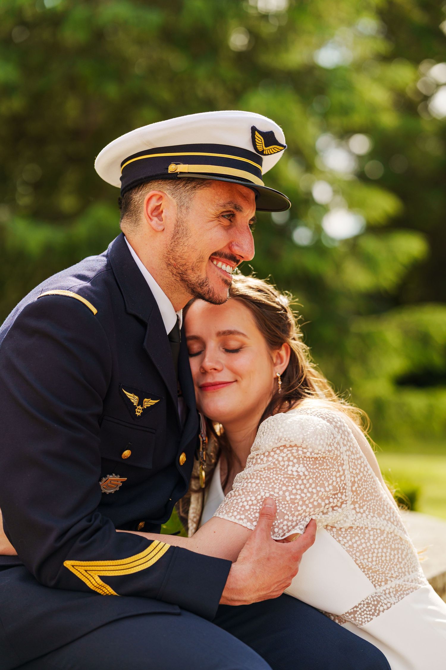 A military officer in uniform embraces a smiling bride outdoors, sharing a tender moment on their wedding day.