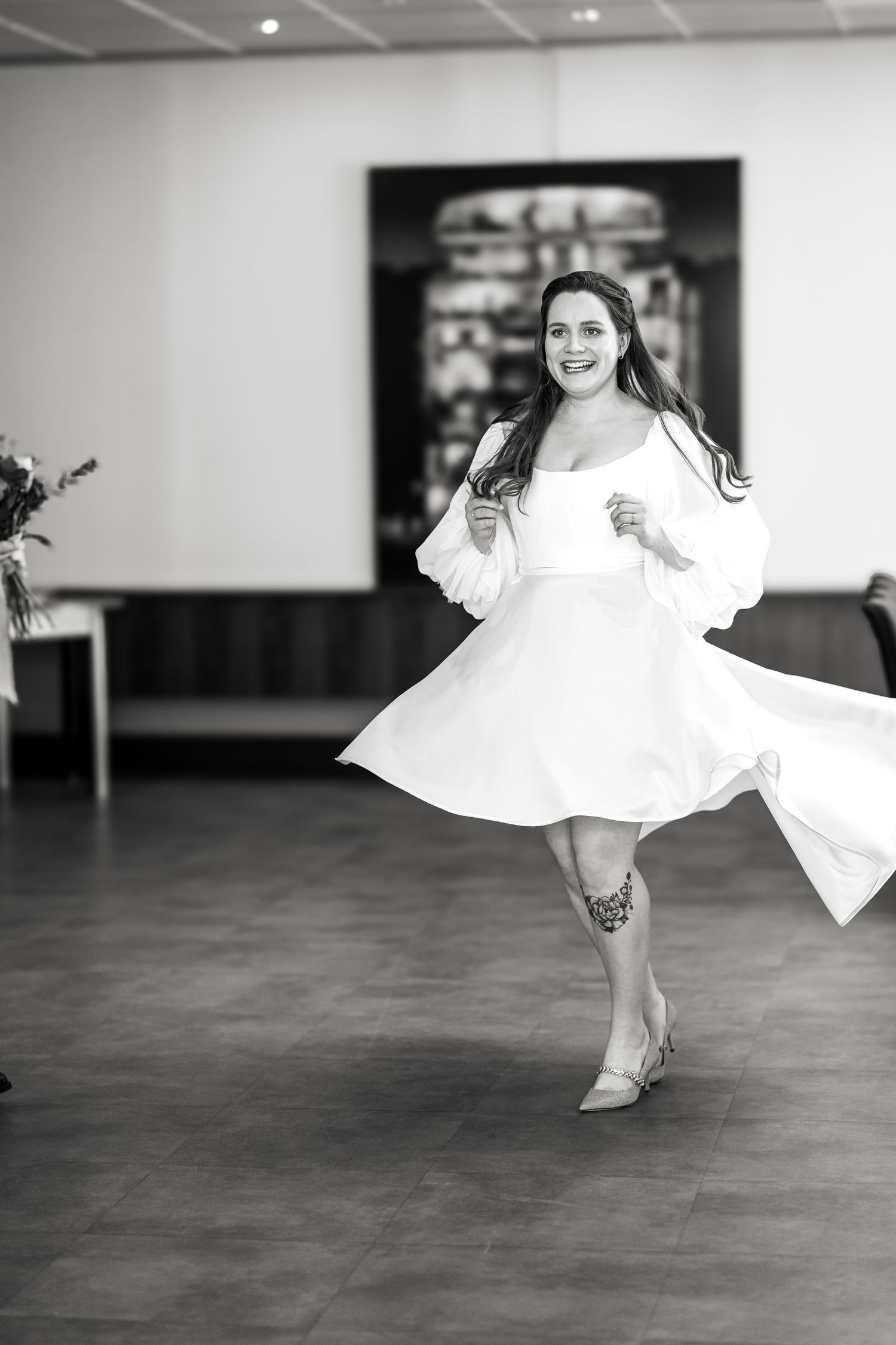 Woman in white dress twirling and smiling in elegant indoor space, black and white photo.