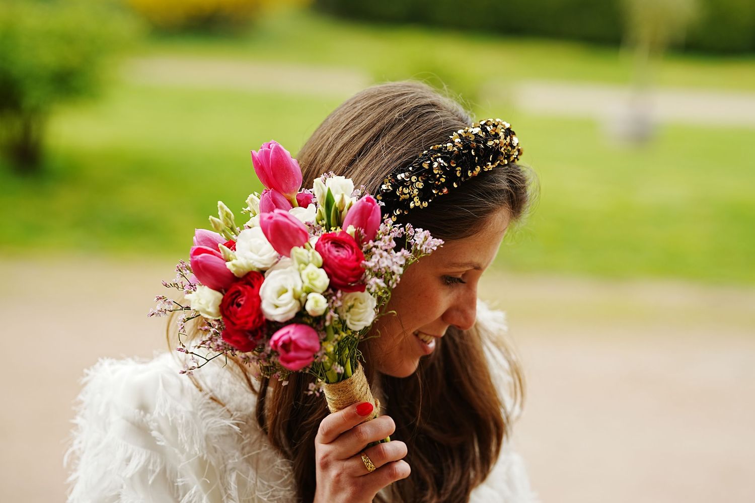 Bride smelling pink tulip bouquet wearing gold crown tiara and white fur wrap outdoors.