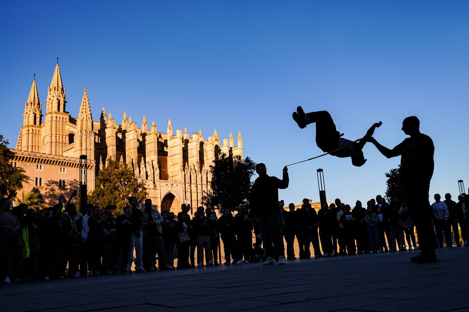 Silhouettes of people photographing a Gothic cathedral against a blue sky at sunset.