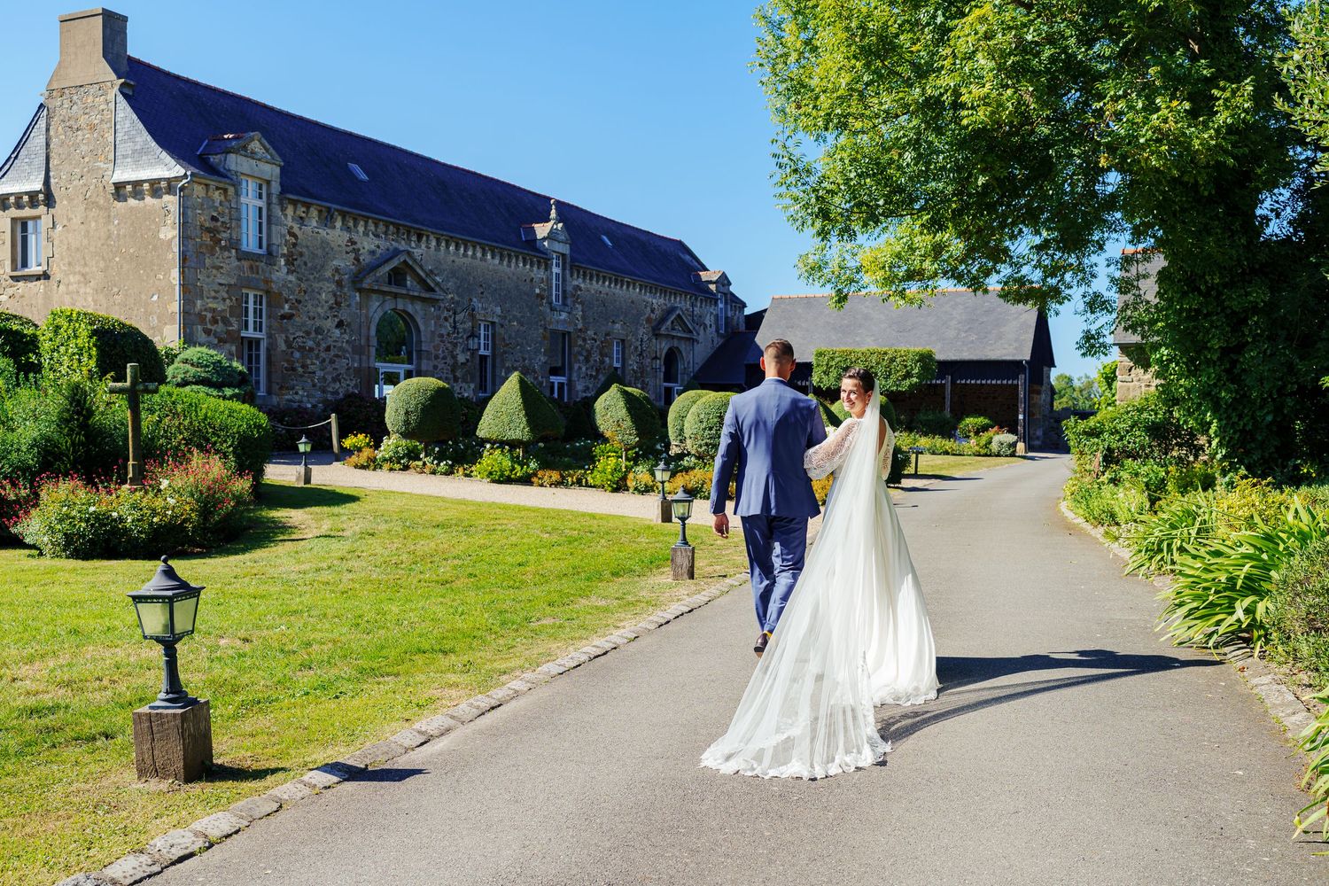 Wedding couple walking along a scenic church pathway surrounded by greenery.