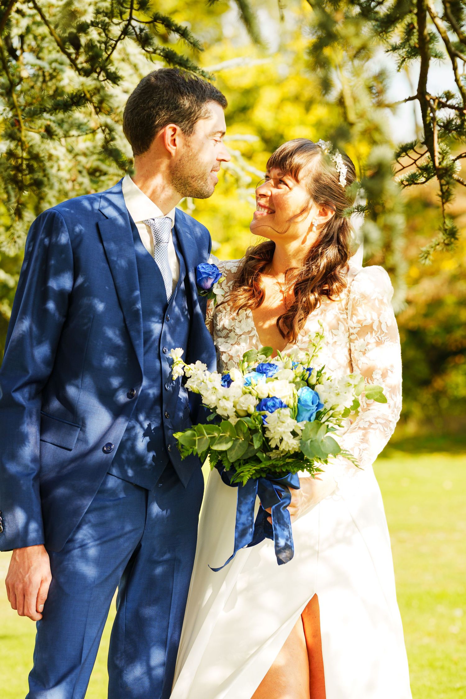 Couple in navy suit and white dress share intimate moments in dappled sunlight.