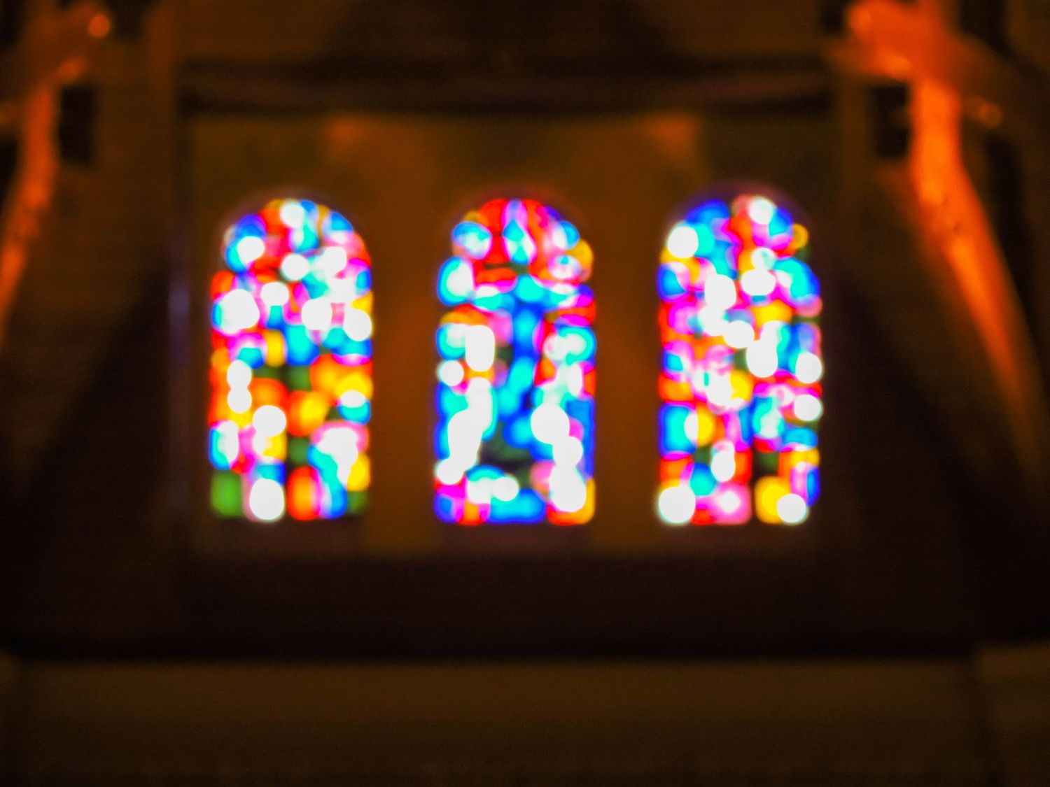Three stained glass church windows glowing with colorful bokeh lights in the darkness.