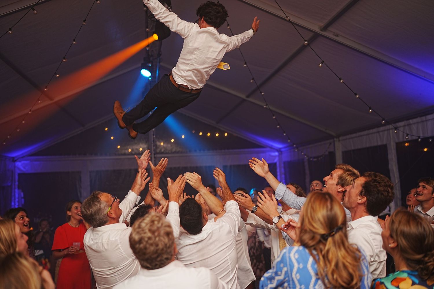 Wedding reception dance floor filled with guests dancing under blue and purple lighting.