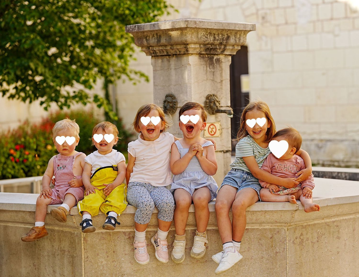 Row of people sitting on stone ledge wearing casual summer clothing and sneakers in outdoor setting.