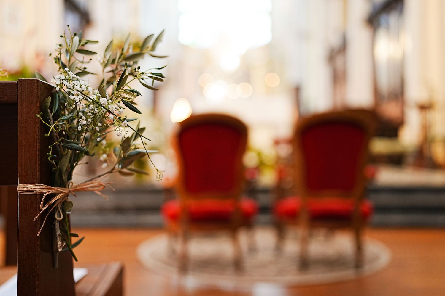 Two red velvet chairs sit in a blurred interior space with a small floral arrangement in the foreground.