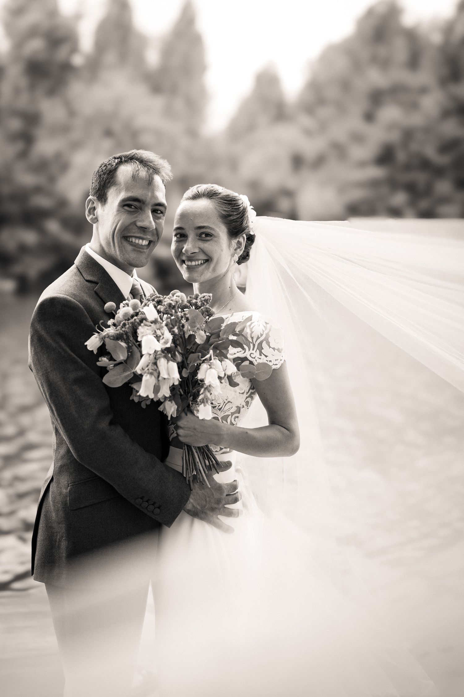 A black and white portrait of a couple sharing a tender moment with a flowing veil and bouquet.